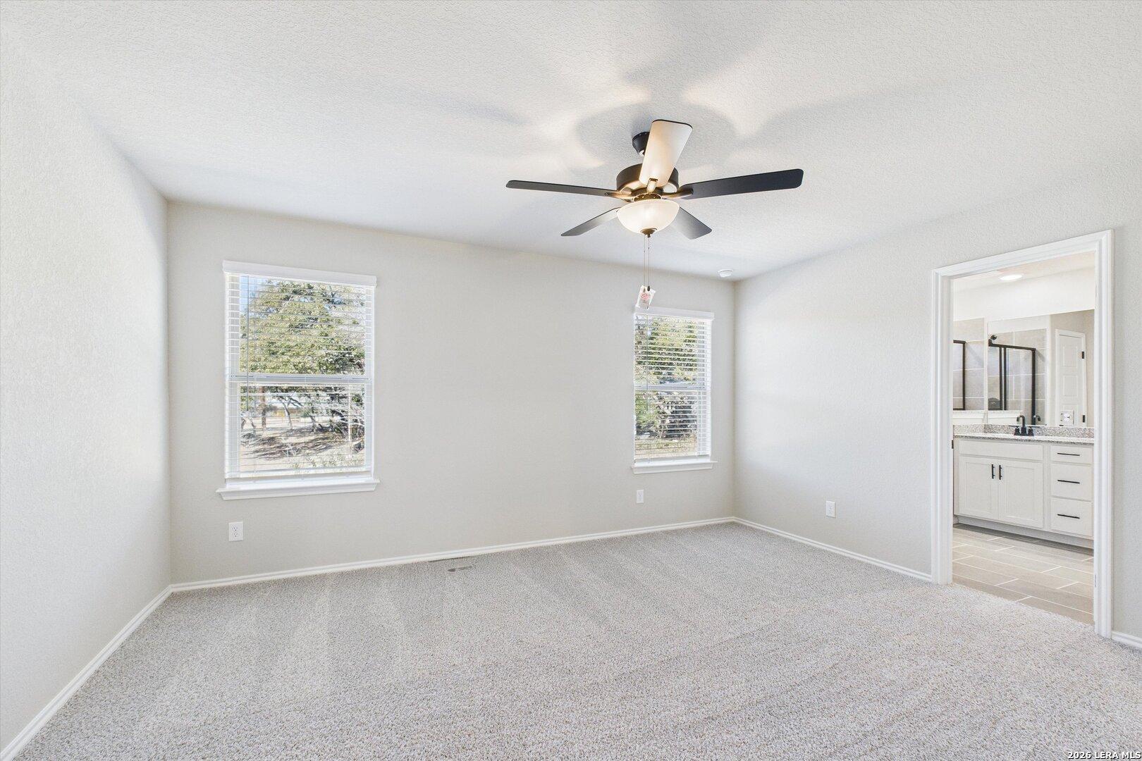 Bright secondary bedroom with ceiling fan, carpet floors, and window views to trees in Davidson Homes The Charlotte A, San Antonio