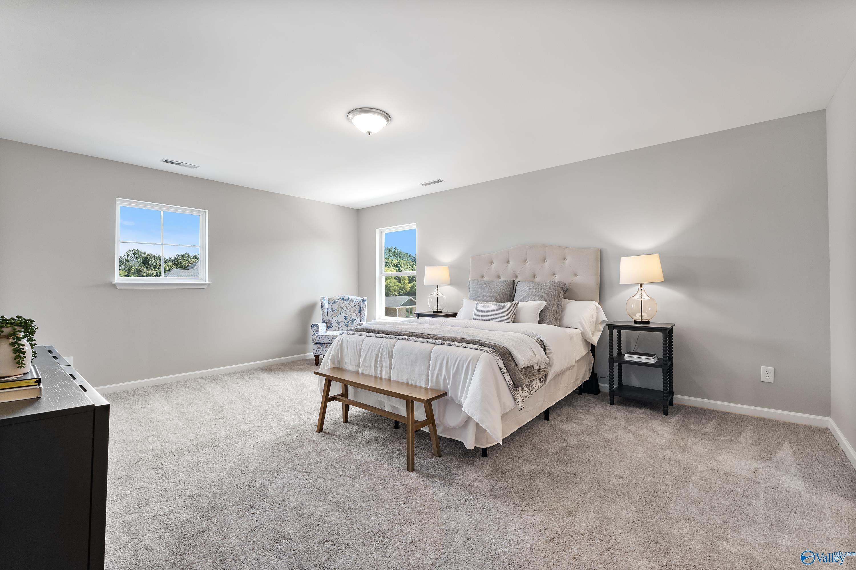 Elegant master bedroom with tufted king bed, gray walls, bedside lamps, and tree-view window in Davidson Homes The Charm, Huntsville, AL