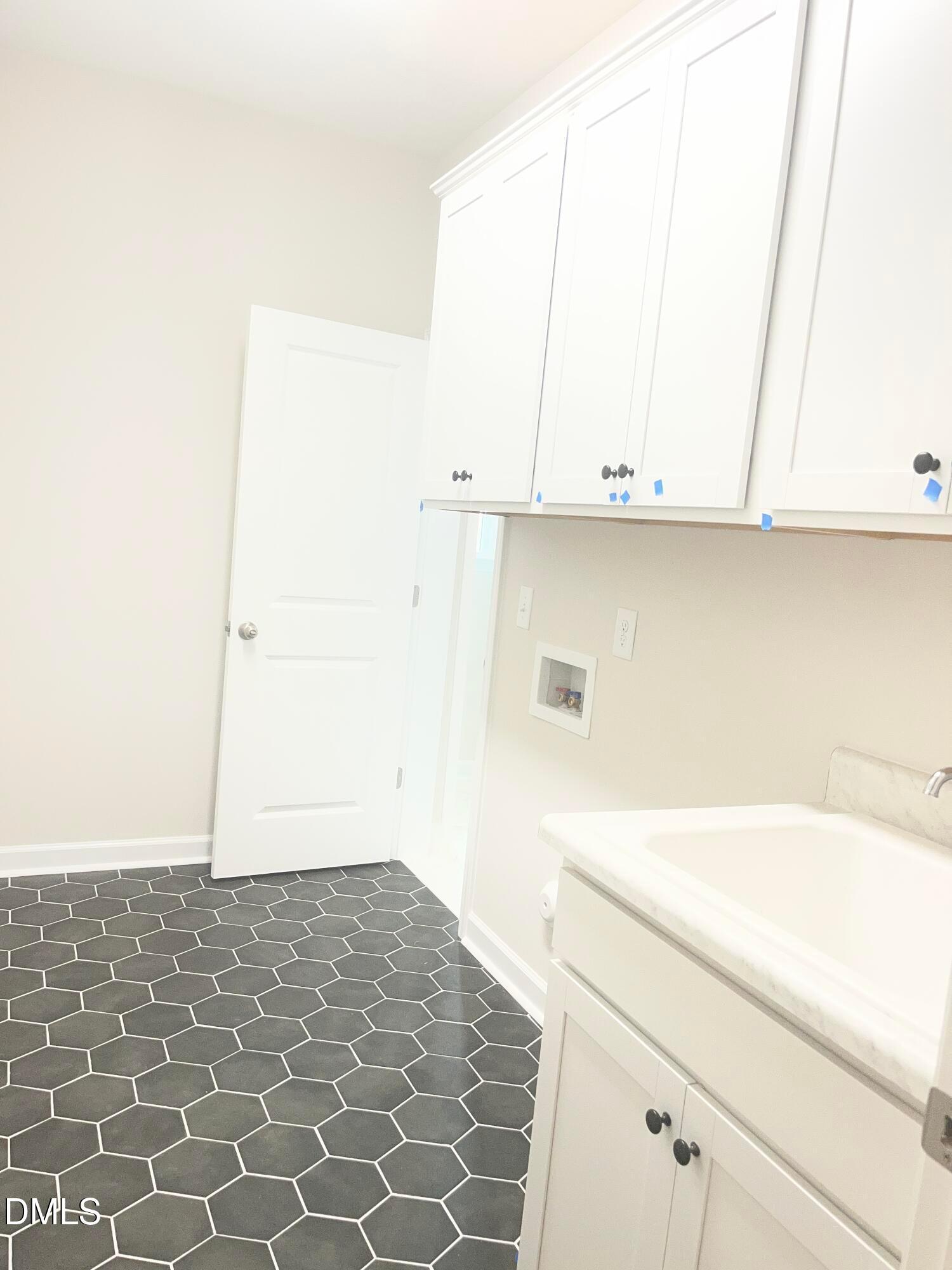 Modern laundry room with white shaker cabinets, gray hexagonal tile floor, and utility sink in Davidson Homes Ashport L, Wake Forest