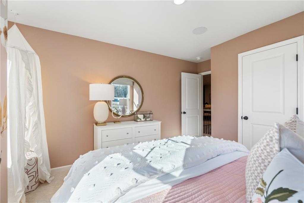 Elegant master bedroom with beige walls, tufted white bed, round mirror, and dresser in Davidson Homes The Marion C, Winder, Georgia