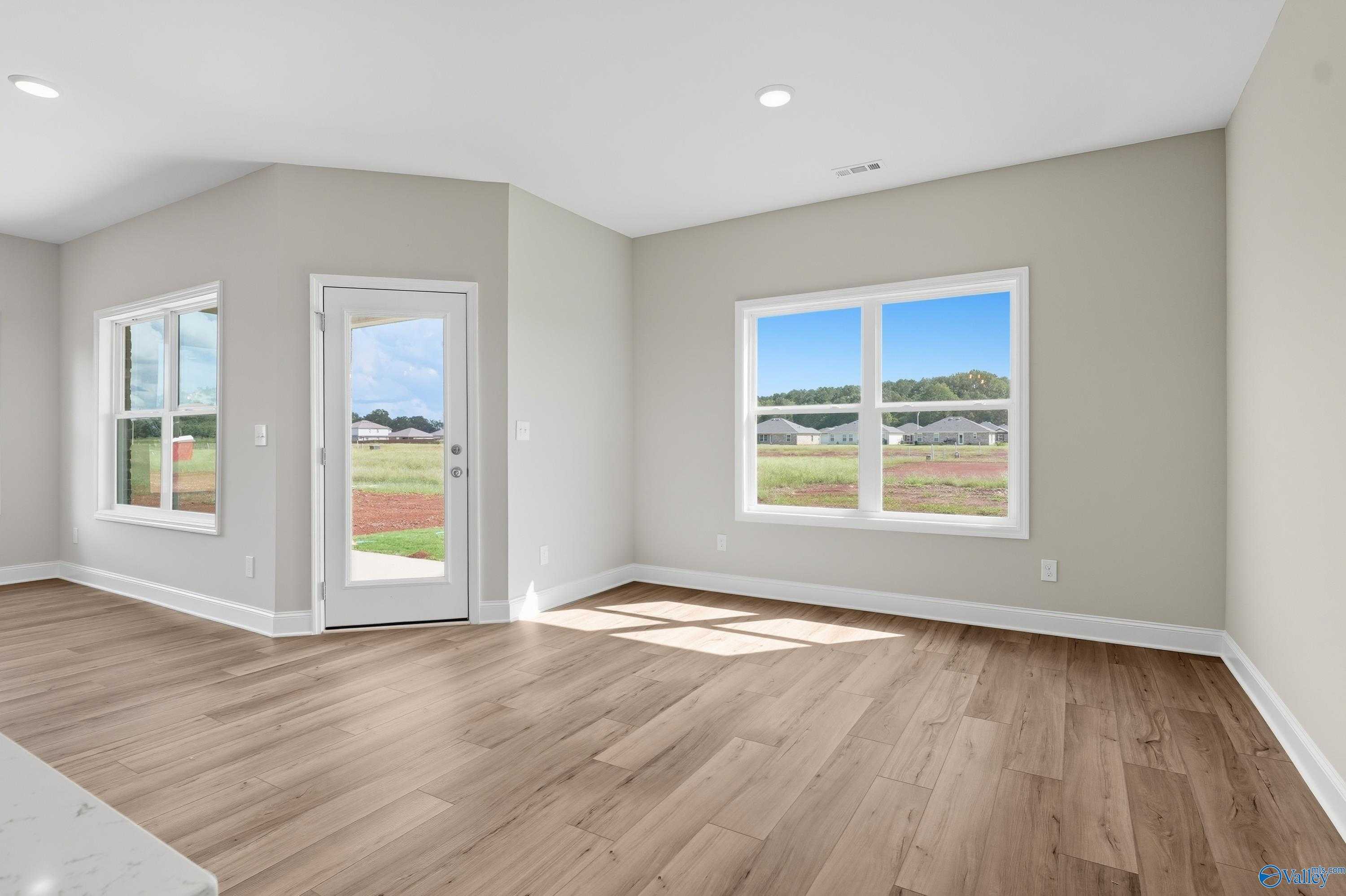 Bright family room with neutral walls, hardwood floors, large windows, and glass door to backyard views in Davidson Homes The Franklin, Meridianville, AL