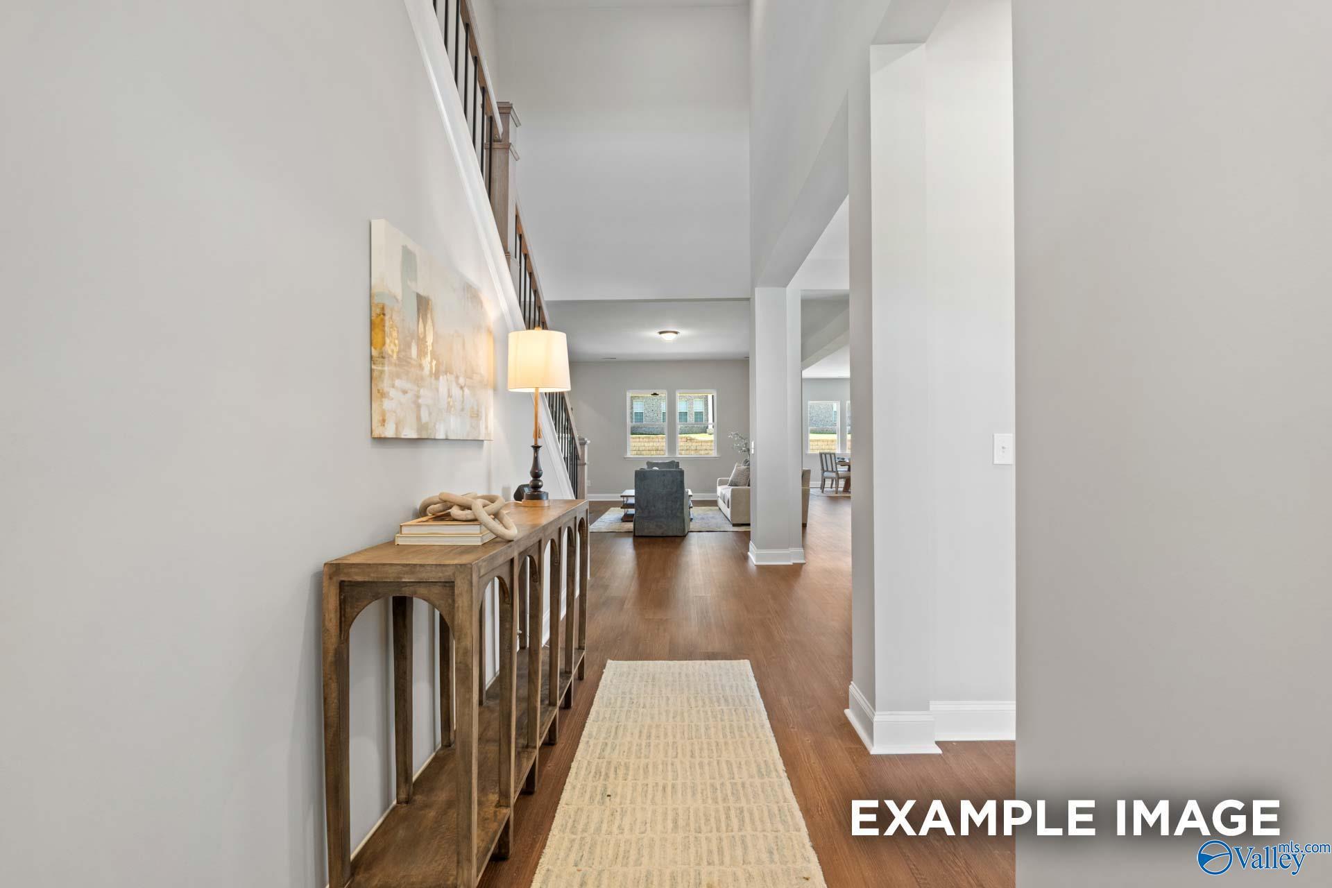 Elegant foyer with wooden console table, abstract painting, iron staircase, and open living area in Evermore Homes The Haven E, Owens Cross Roads, AL