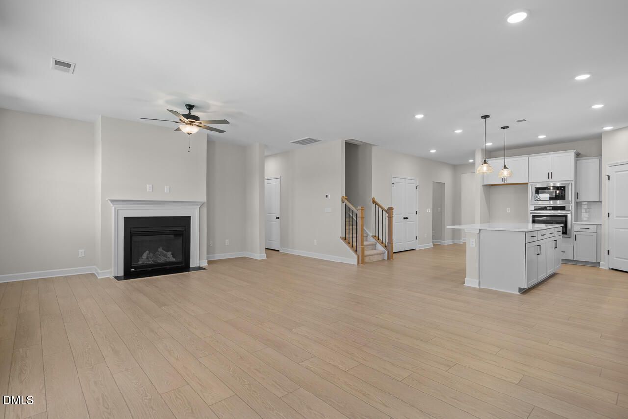 Open-concept living room with fireplace and white kitchen island in The Ashport M, Davidson Homes, Wendell Ridge, NC