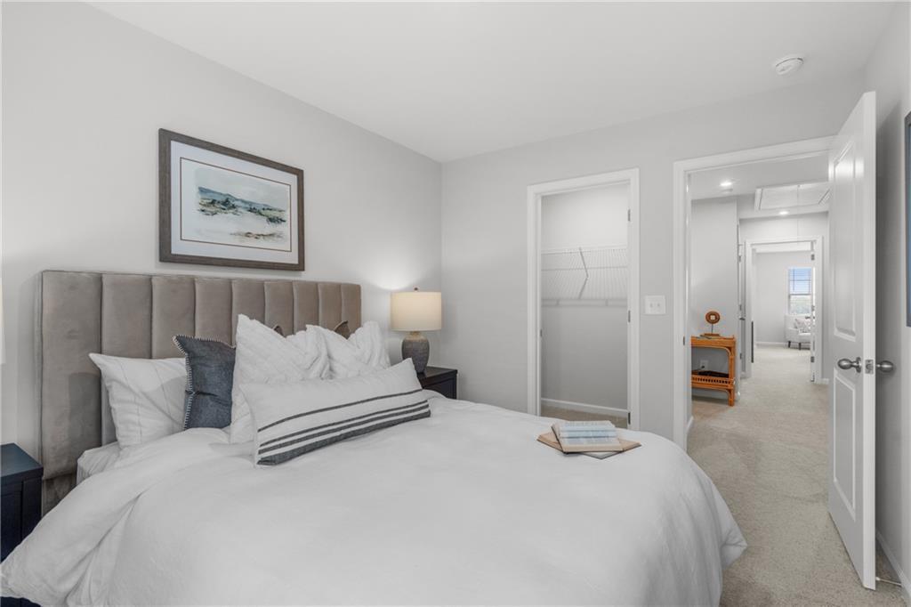 Elegant master bedroom with tufted gray headboard, white bedding, pillows, nightstand lamp, and en-suite bath in Davidson Homes The Durant B, Emerson, Georgia