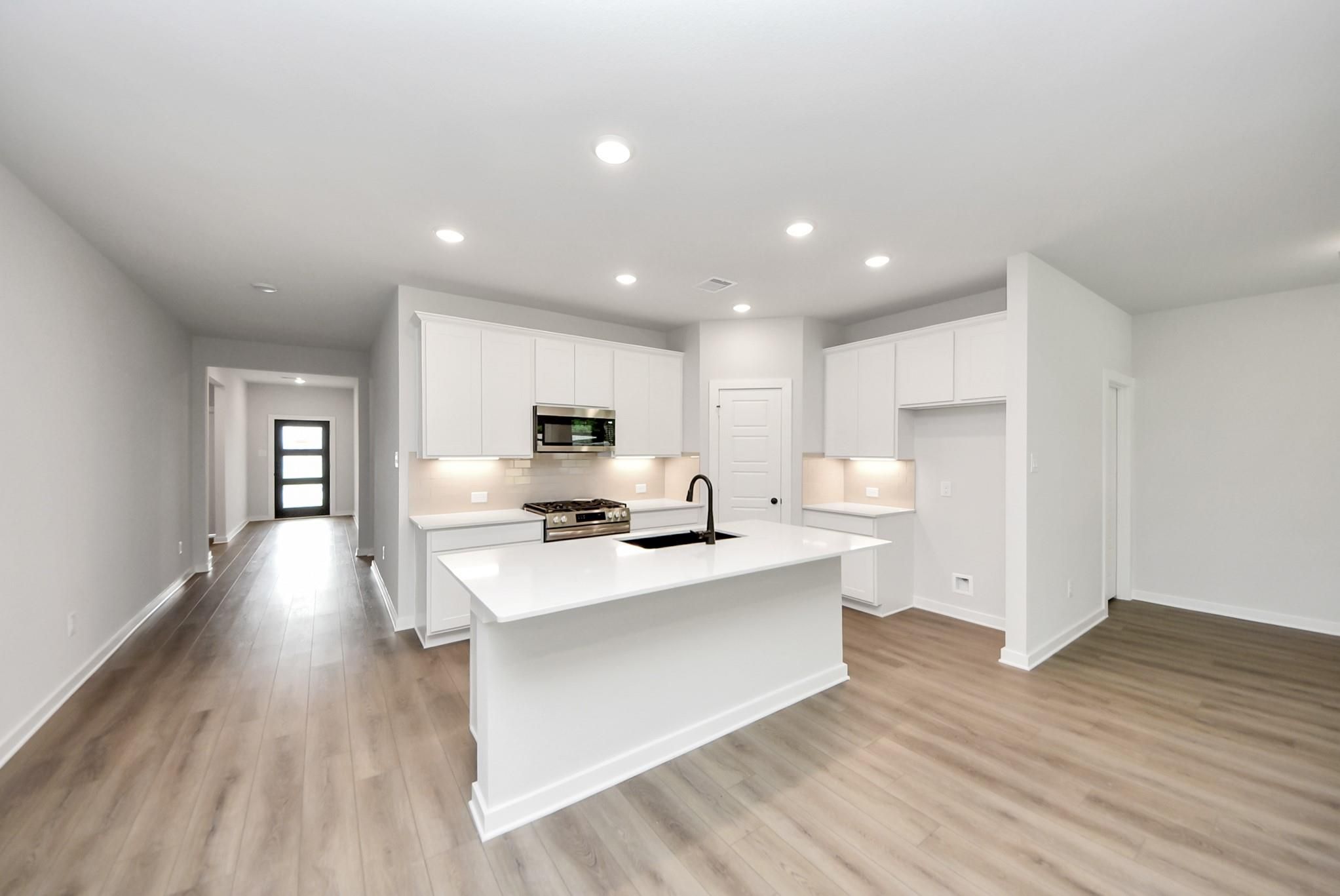 Modern kitchen with white cabinets, quartz island, and stainless appliances in The Daphne F plan at Sundance Cove, Crosby.