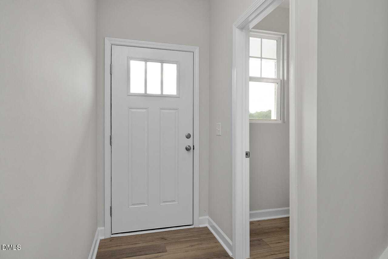 Modern entryway with white paneled front door, glass sidelight, gray walls, and hardwood floors in Davidson Homes The Warren, Fuquay-Varina