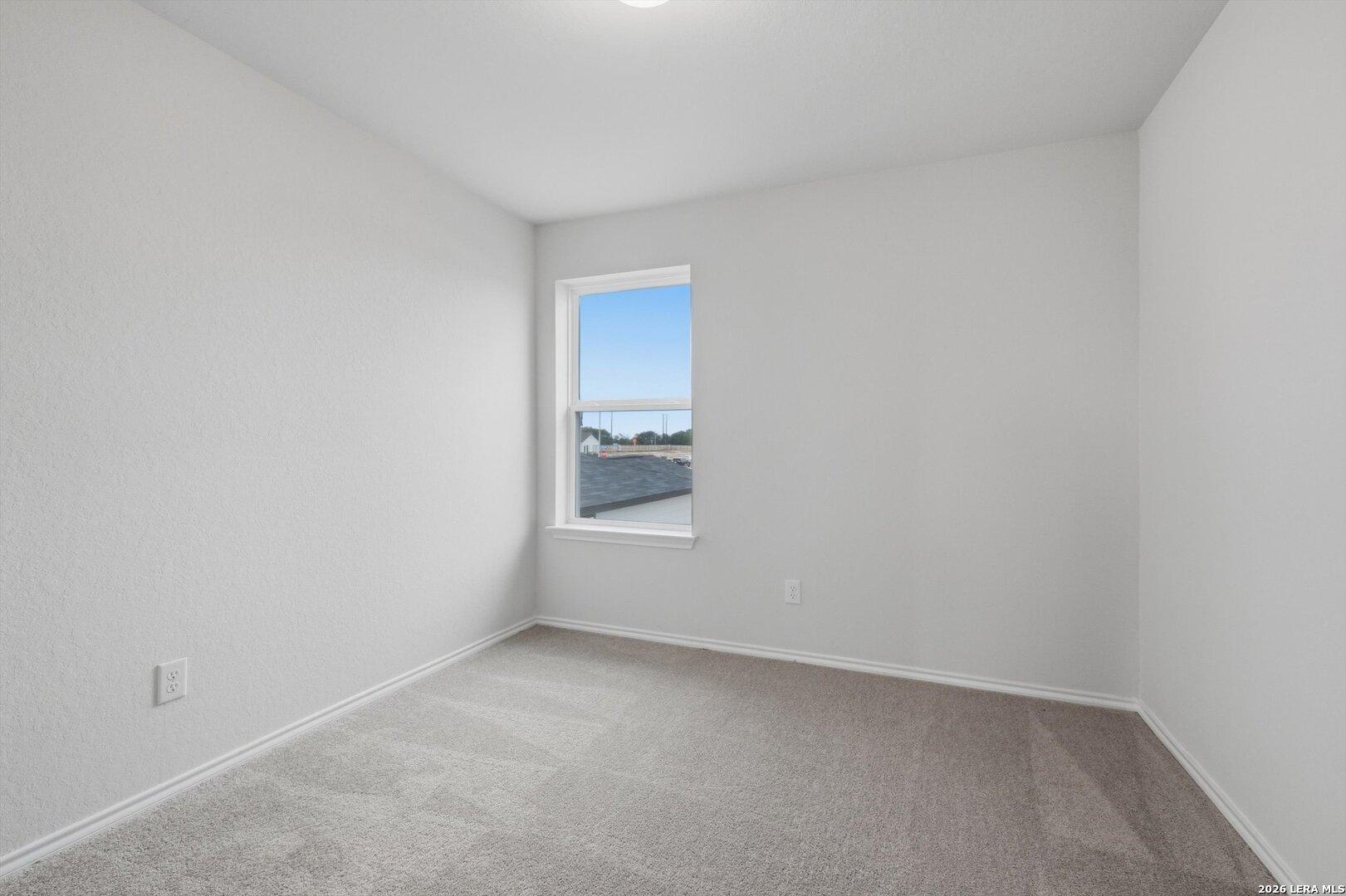 Empty bedroom with white walls, beige carpet, large window overlooking construction in Davidson Homes The Blanco C, San Antonio