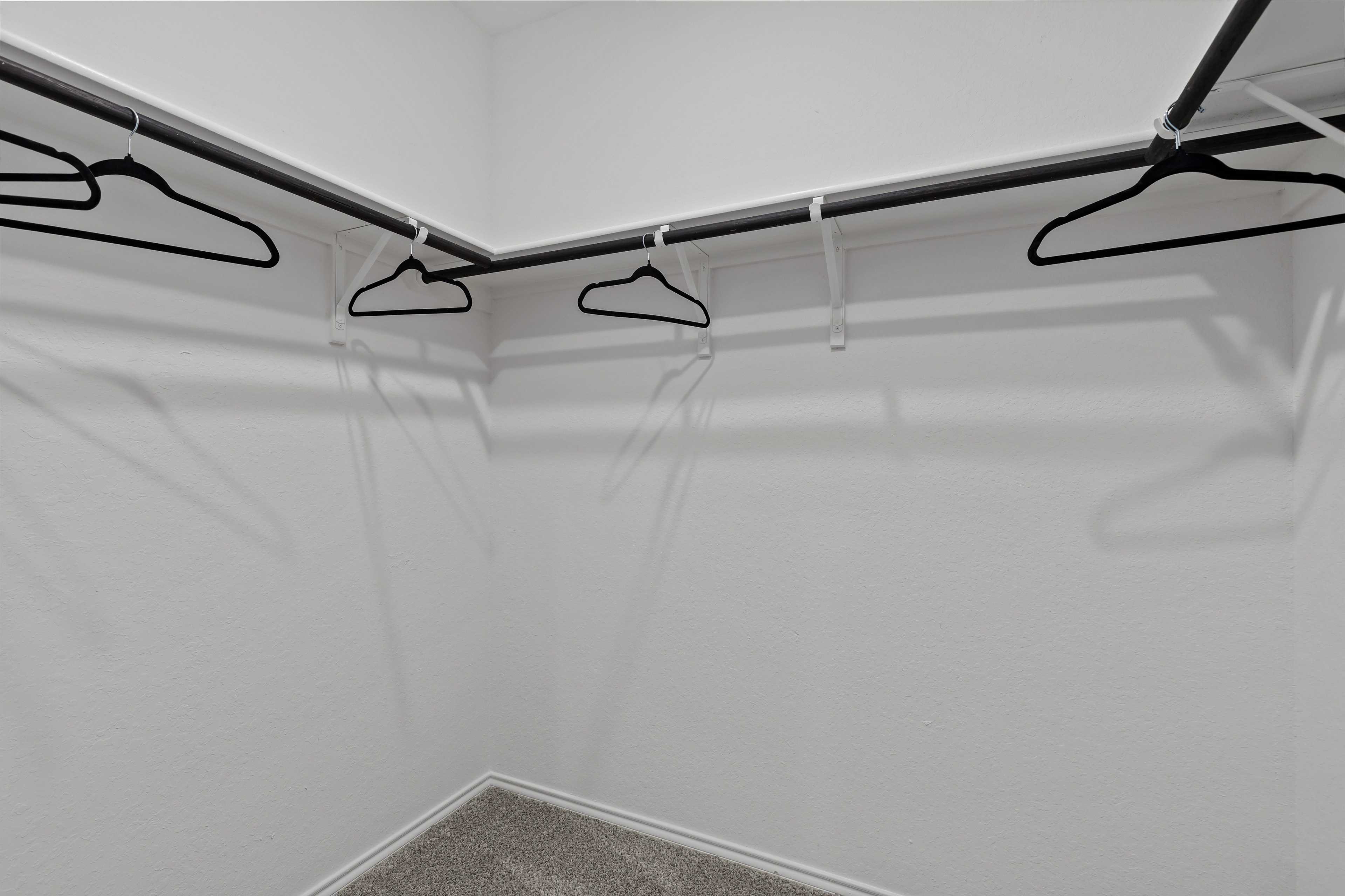 Spacious walk-in closet in The Douglas C by Davidson Homes, featuring dual hanging rods, wooden hangers, and neutral walls