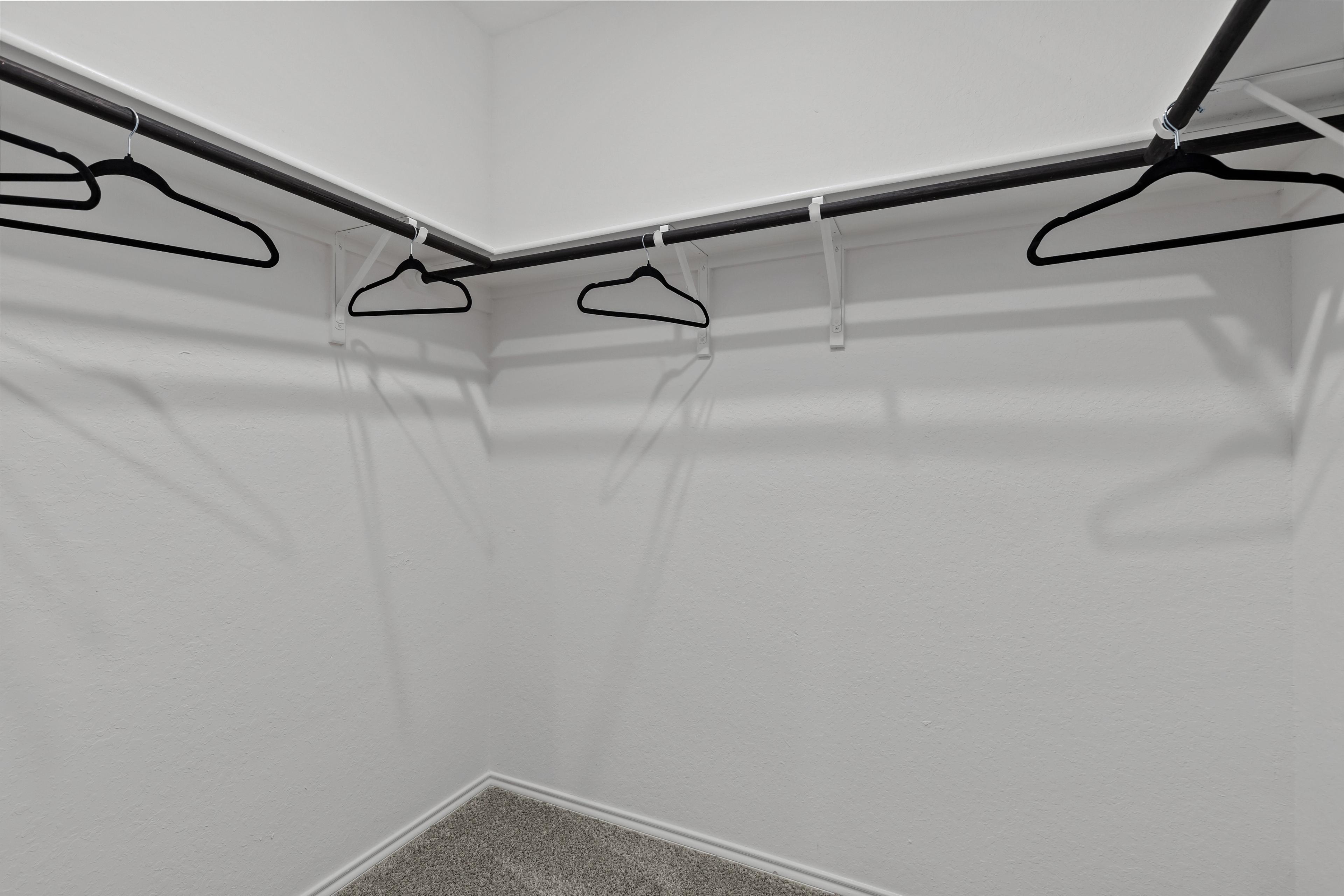 Spacious walk-in closet in The Douglas F master suite featuring white walls, corner hanging rods, and black hangers