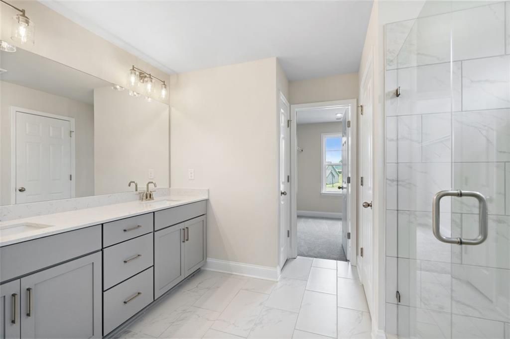 Elegant master bathroom with double vanity, frameless glass shower, and white tile floor in The Willow D home at Wehunt Meadows, Hoschton GA