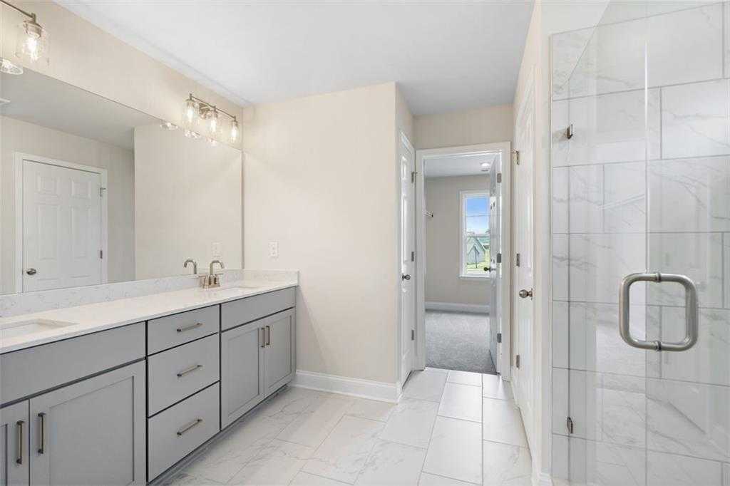 Elegant master bathroom with double vanity, frameless glass shower, and white tile floor in The Willow D home at Wehunt Meadows, Hoschton GA