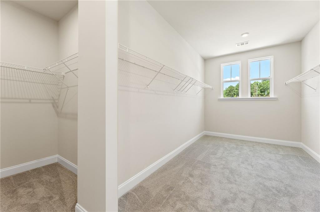 Spacious walk-in closet with white wire shelving, beige walls, carpeted floor, and double windows overlooking trees in Davidson Homes The Danbury C, Buford, GA