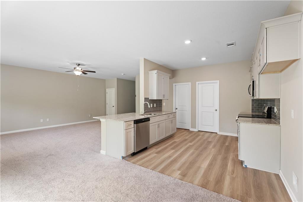 Modern open-concept kitchen with white cabinets, island sink, and adjacent living area in The Bartlett 3-bedroom home, Phenix City, Alabama