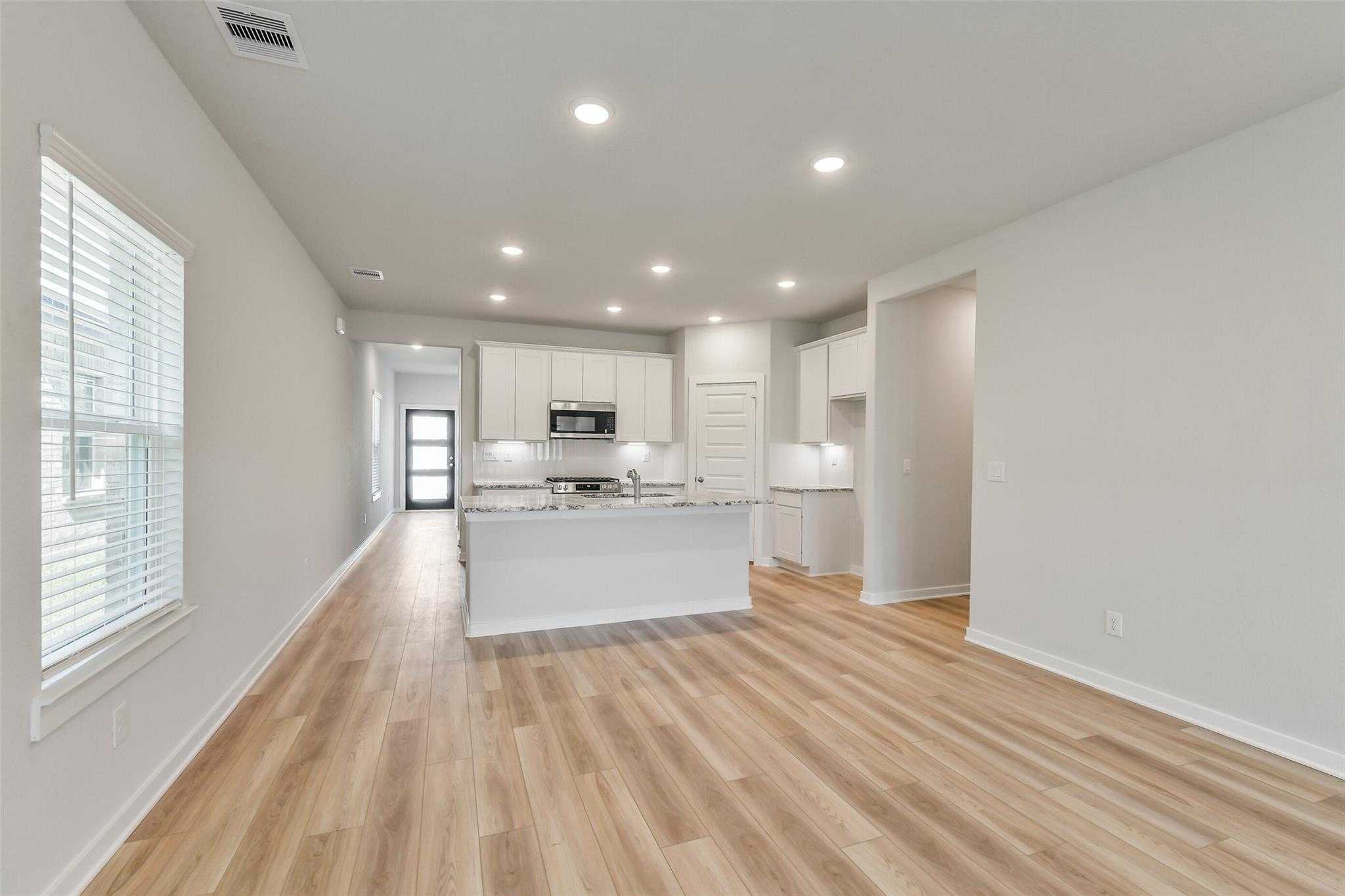 Modern hallway with wood-look flooring leading to bright white kitchen island and cabinets in The Rio Grande H, Magnolia, Texas