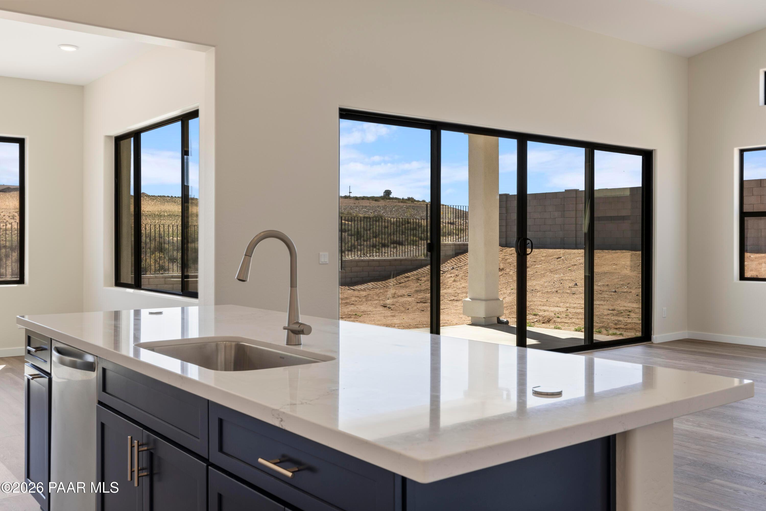 Modern kitchen island with white quartz counters, dark cabinets, and sliding doors to desert mountain view in Prescott AZ home