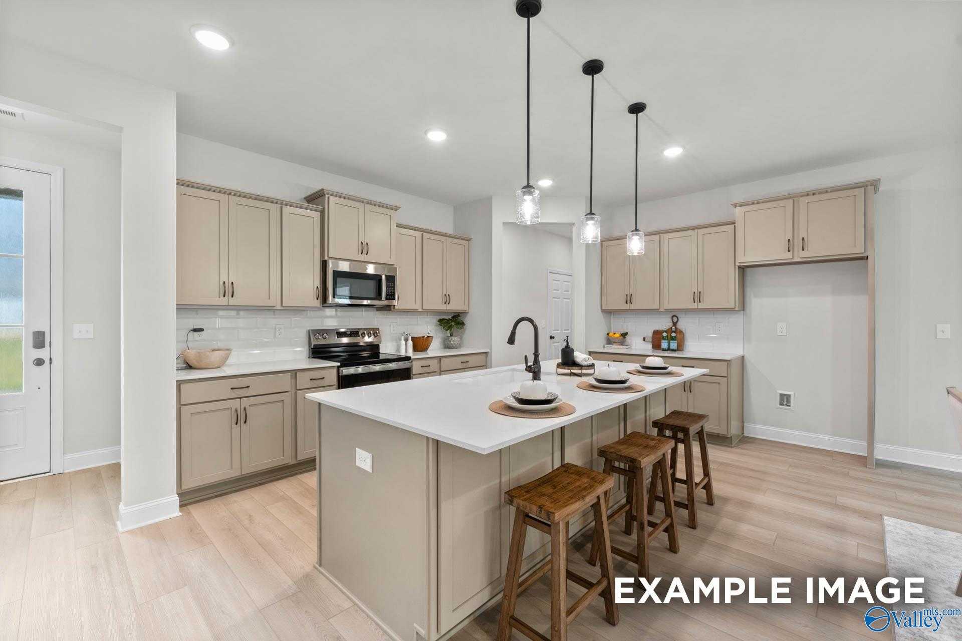 Modern open-concept kitchen with beige cabinets, white quartz island, stainless appliances, and wood bar stools in The Kirkland floor plan, Decatur AL