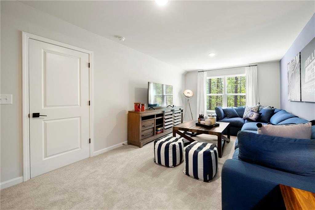 Cozy family room featuring blue L-shaped sofa, wooden TV console, and large windows in Davidson Homes The Hickory B, Riverwood, Dallas, Georgia