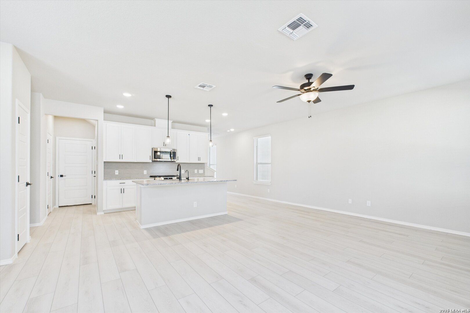 Modern open-concept kitchen with white shaker cabinets, large island, stainless appliances, and ceiling fan in Davidson Homes The Charlotte A, San Antonio