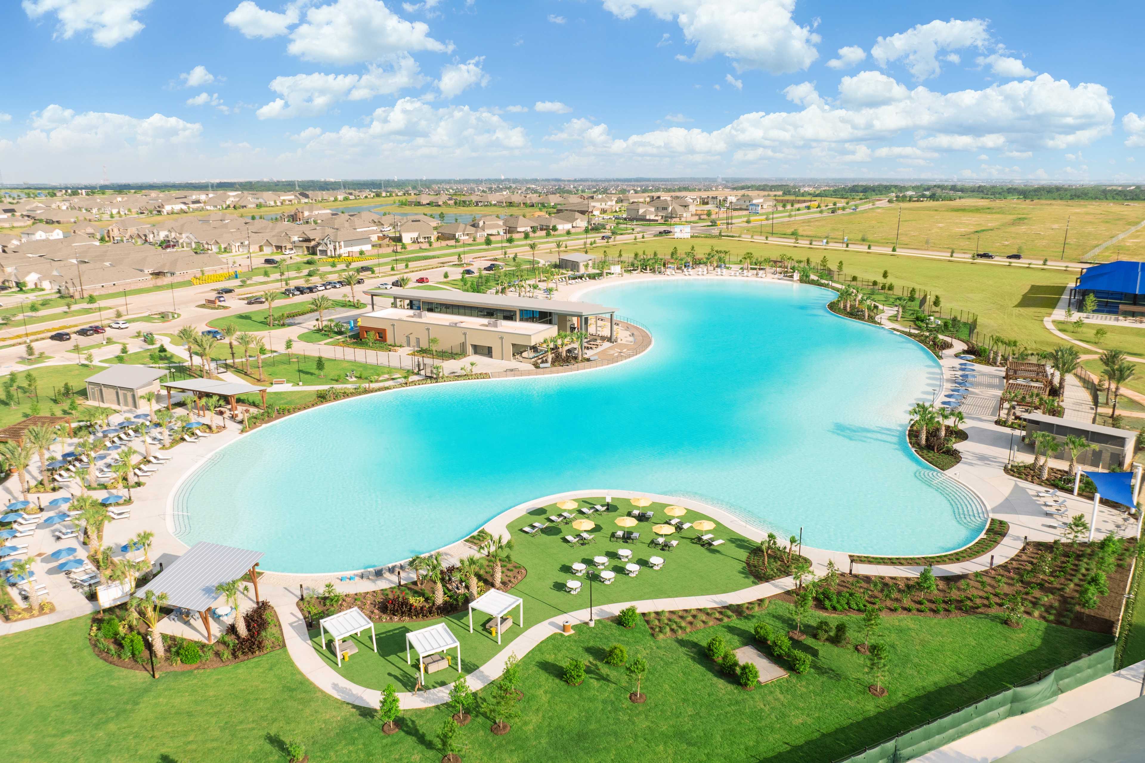Aerial view of resort-style lagoon pool at Sunterra in Katy Texas with lounge seating umbrellas and palm trees