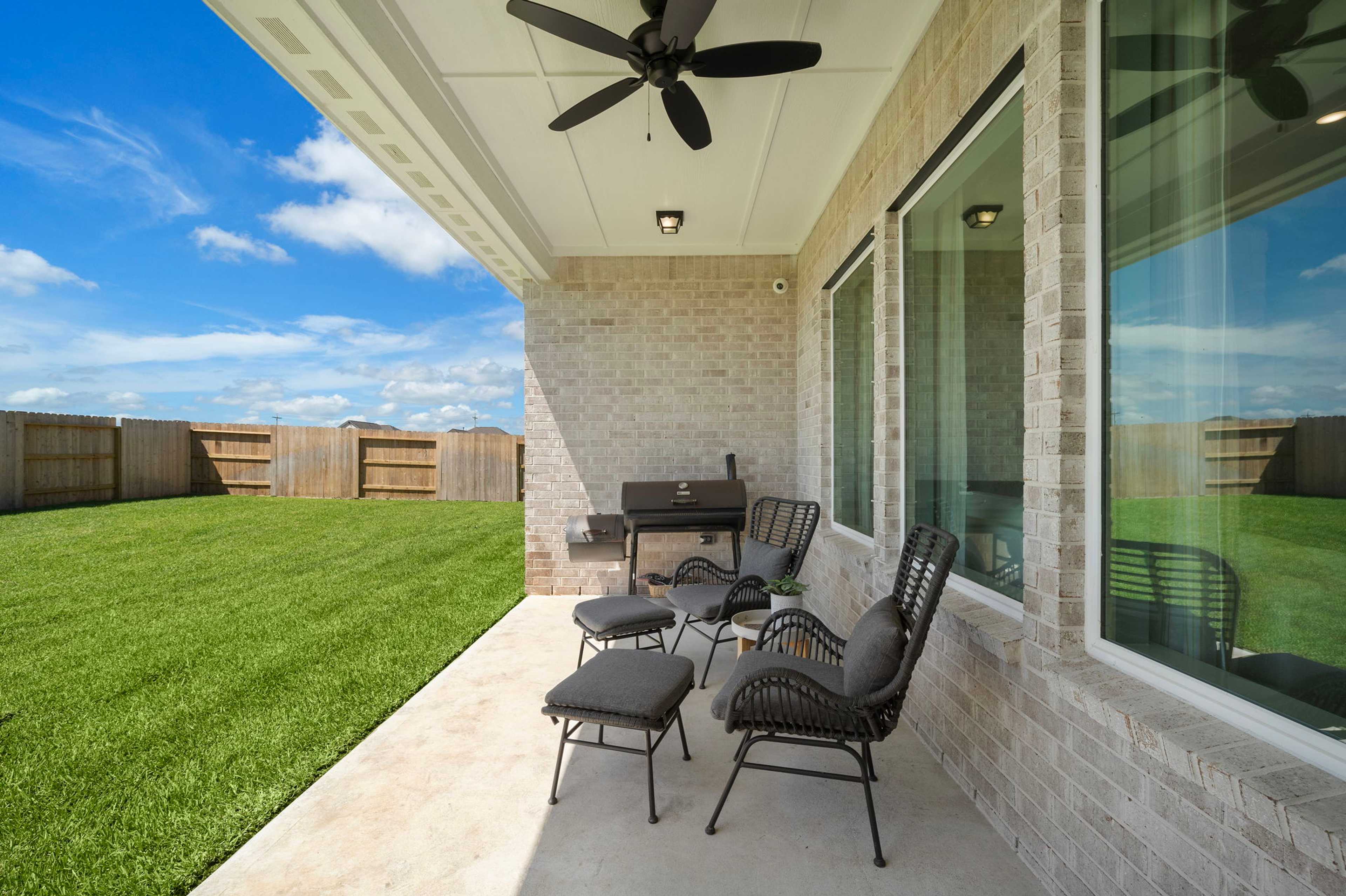 Spacious covered patio at Lago Mar in Texas City TX with brick walls, ceiling fan, wicker chairs, grill and lush green lawn