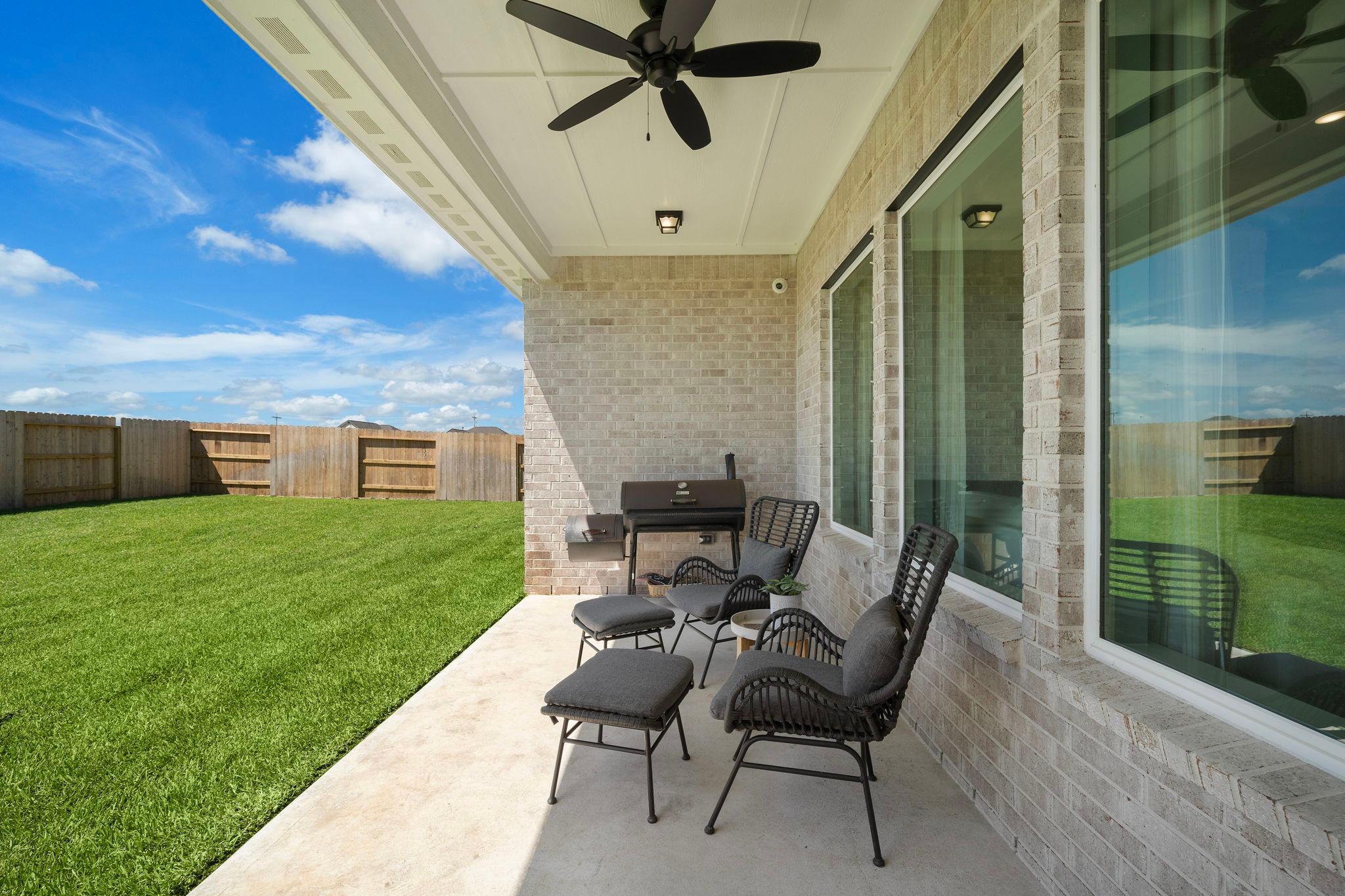 Spacious covered patio at Lago Mar in Texas City TX with brick walls, ceiling fan, wicker chairs, grill and lush green lawn