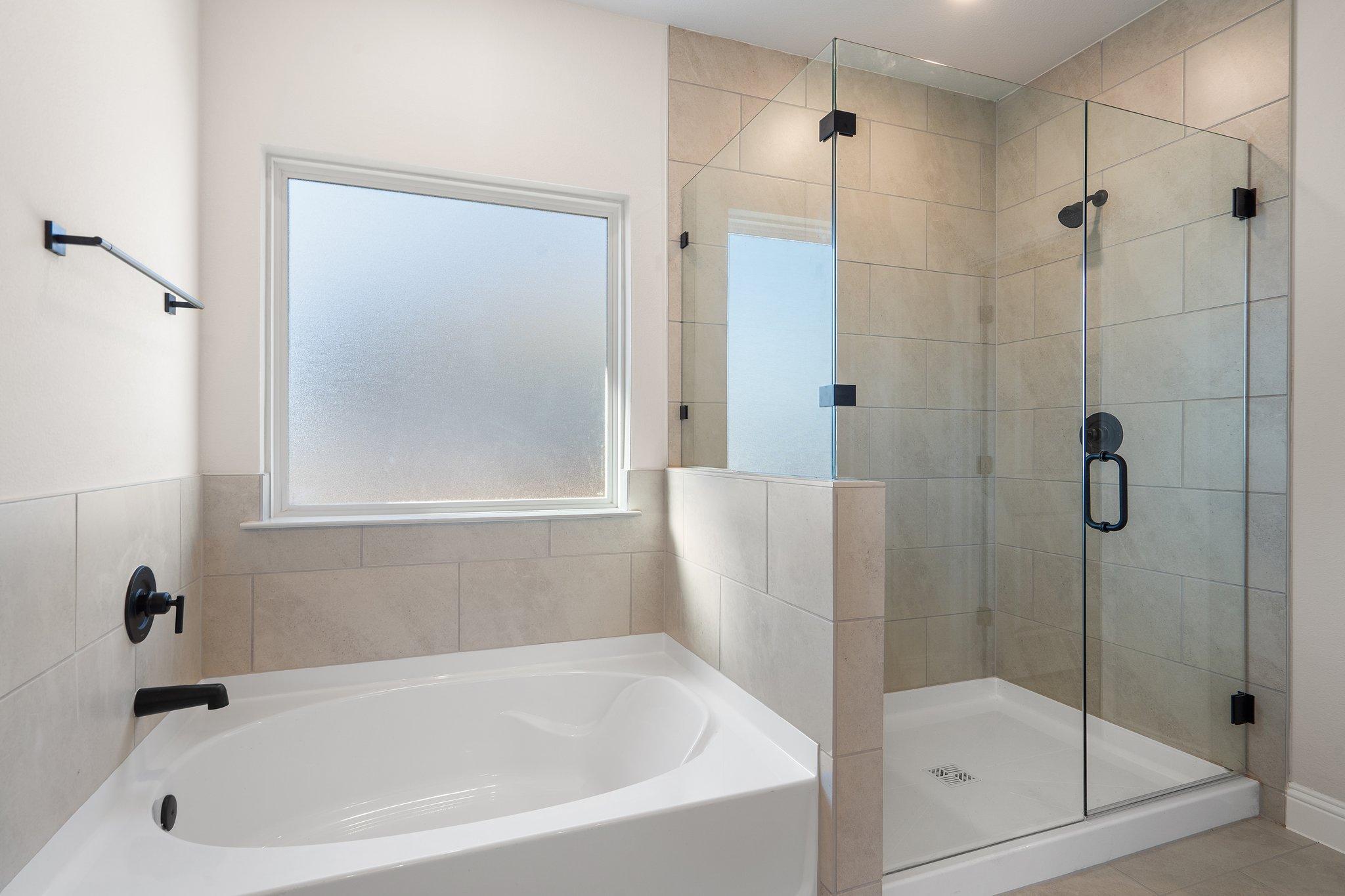 Master suite bathroom in The Holly F featuring a soaking tub and separate glass-enclosed walk-in shower with tile surround.