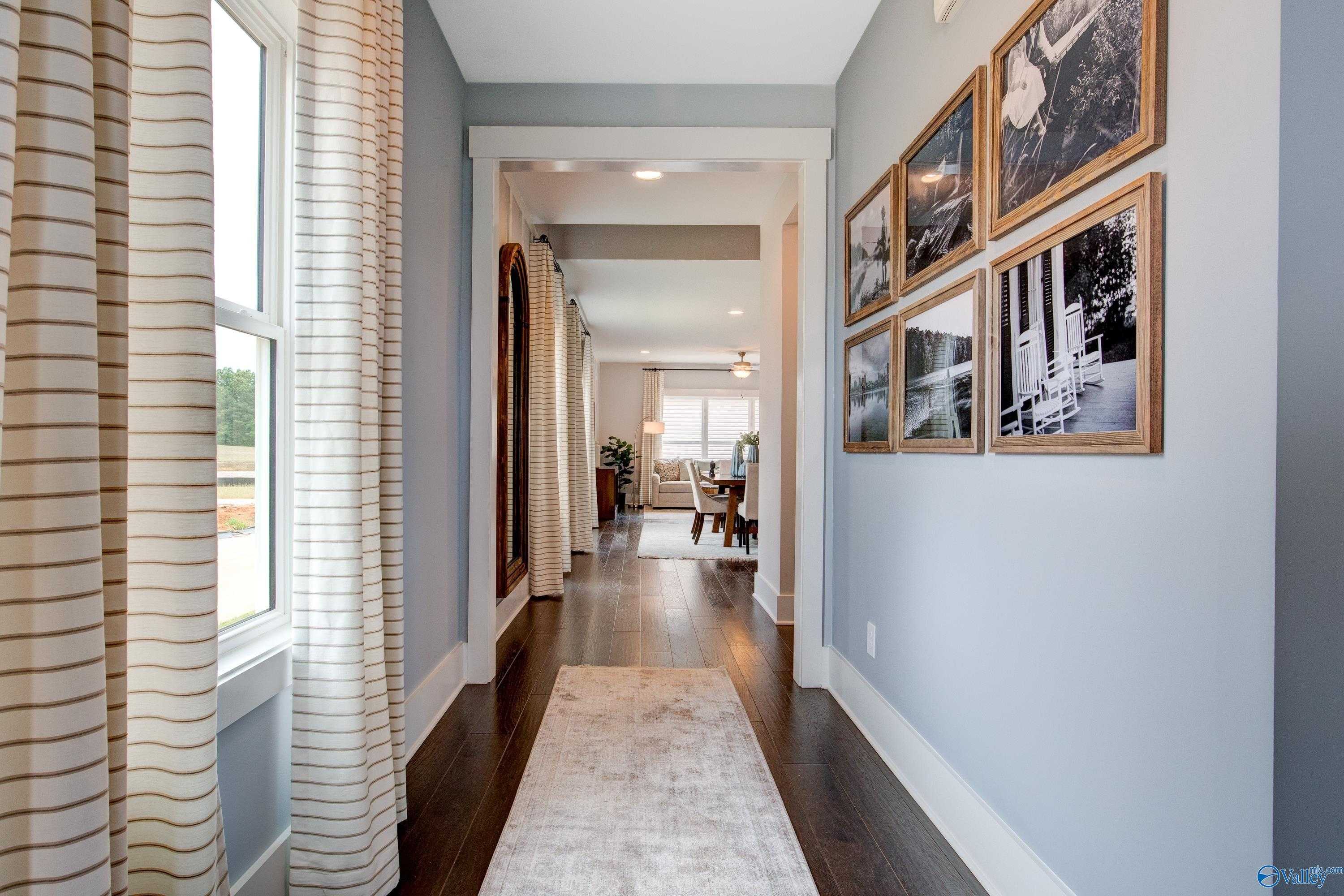 Elegant hallway with light blue walls, striped curtains, black-and-white art, hardwood floors in Davidson Homes The Covington C, Decatur, Alabama