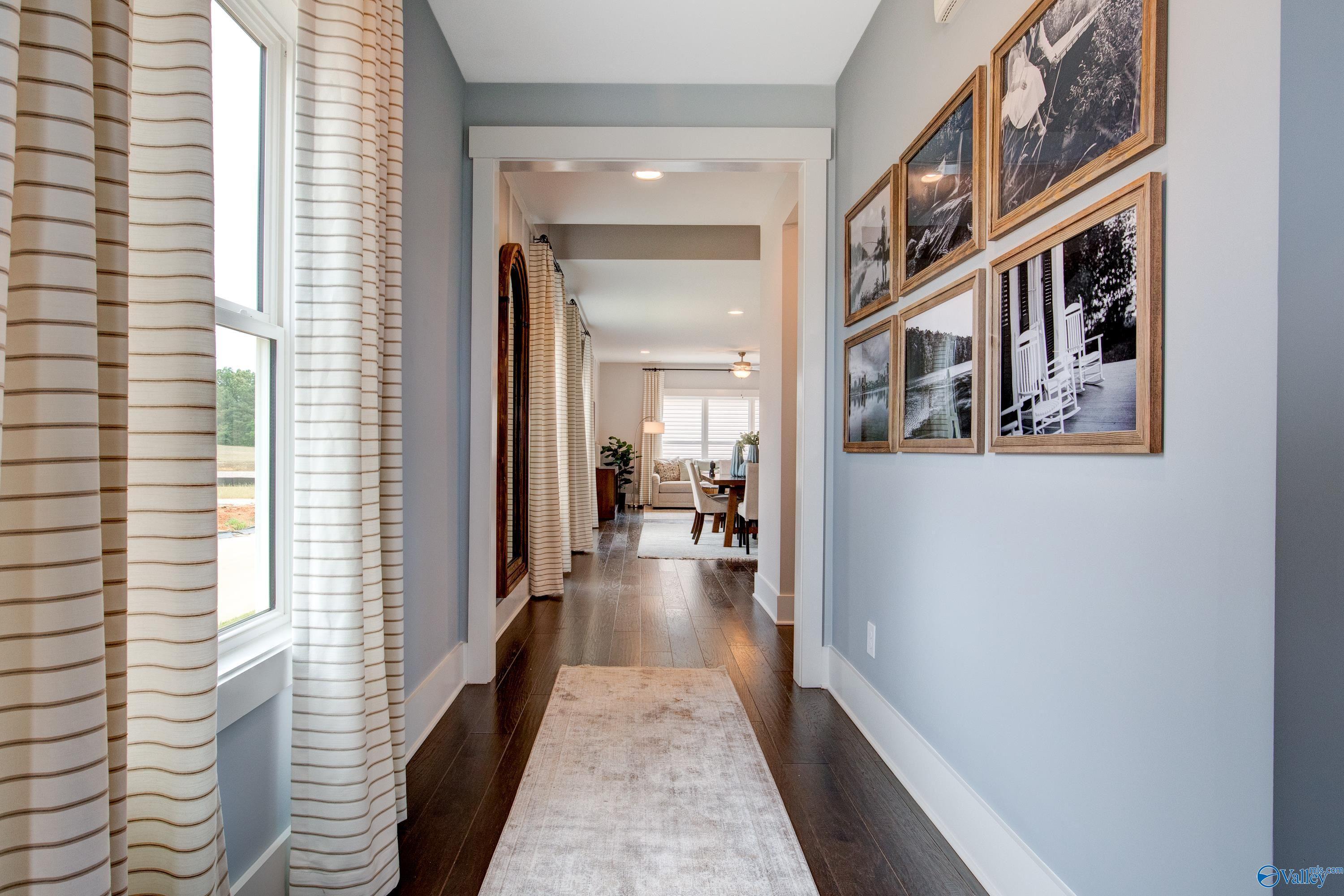 Elegant hallway with light blue walls, striped curtains, black-and-white art, hardwood floors in Davidson Homes The Covington C, Decatur, Alabama