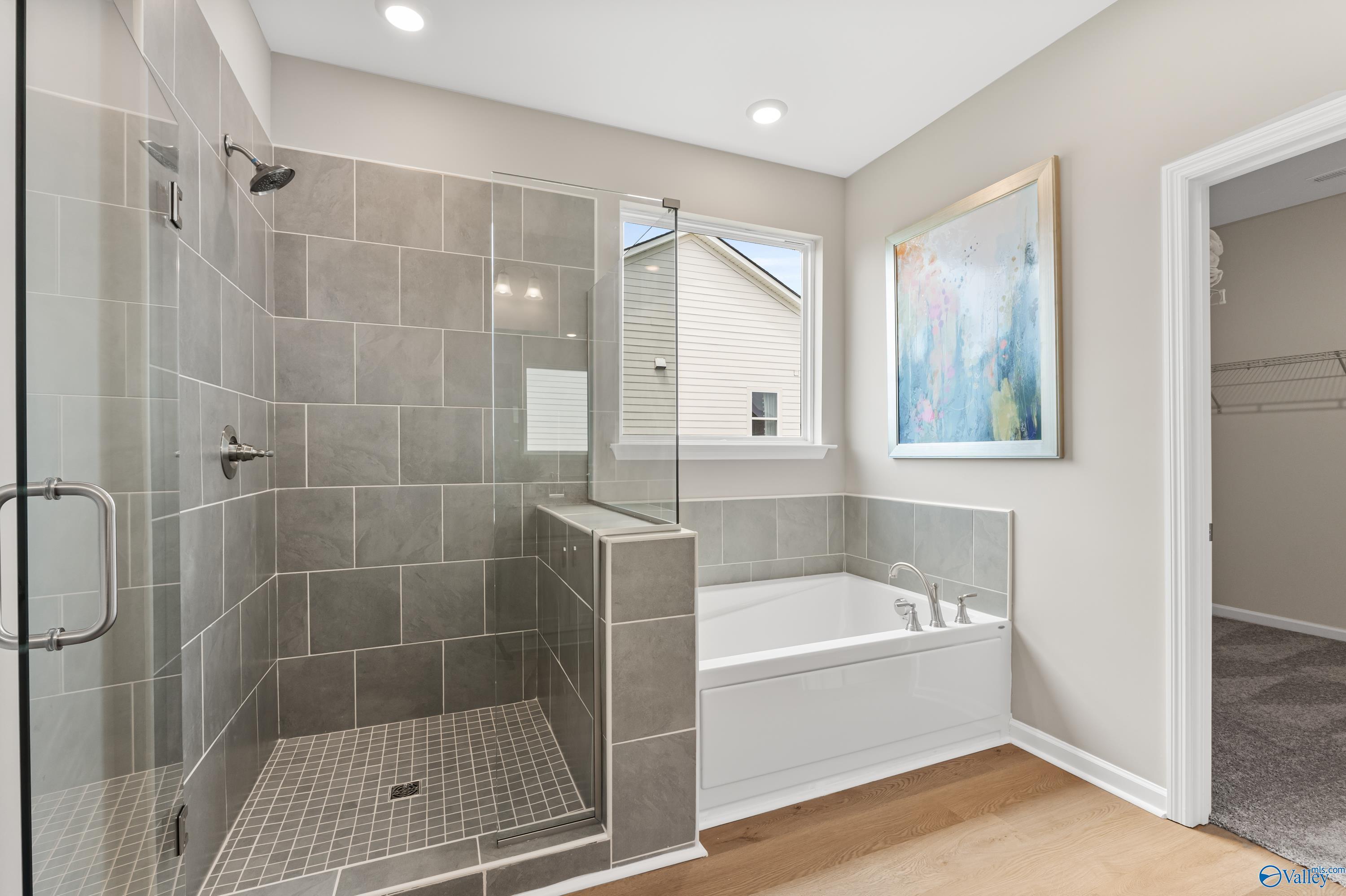 Luxurious master bath with gray tiled walk-in shower, freestanding tub, and walk-in closet in Davidson Homes The Sanctuary, Athens AL