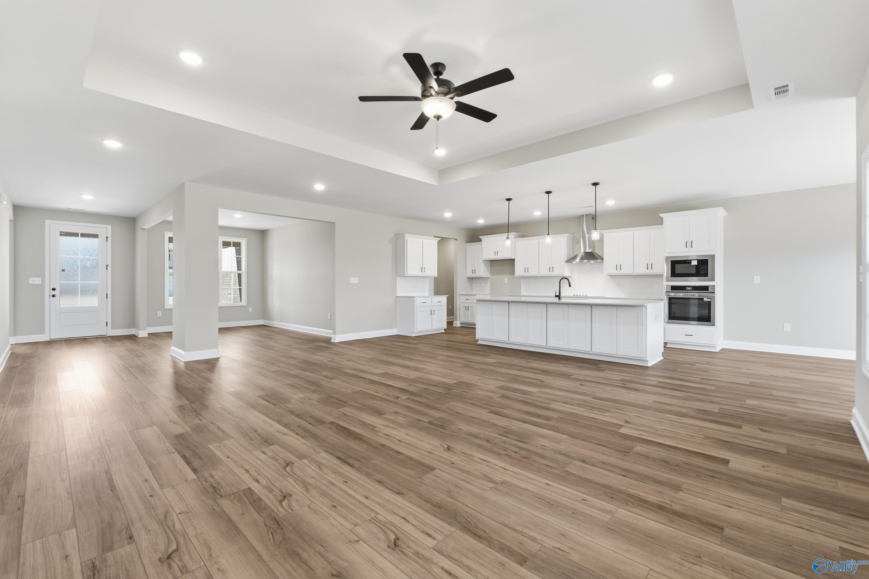 Open-concept kitchen-living area with hardwood floors, white cabinets, island sink, and ceiling fan in Davidson Homes The Finleigh, Meridianville, AL