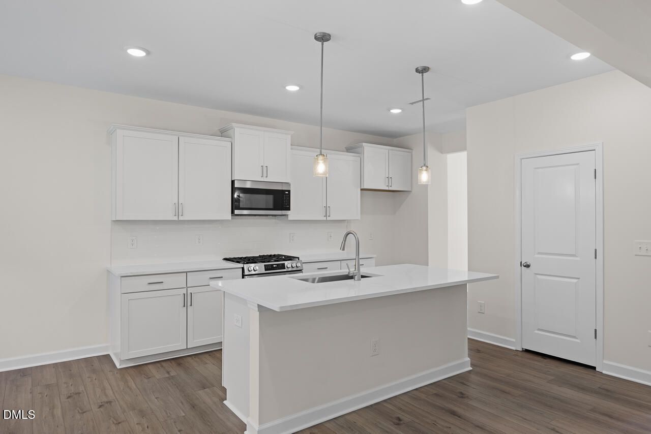 Modern white kitchen with island, pendant lights, stainless gas range, and hardwood-style flooring in Davidson Homes The Willow B, Zebulon NC