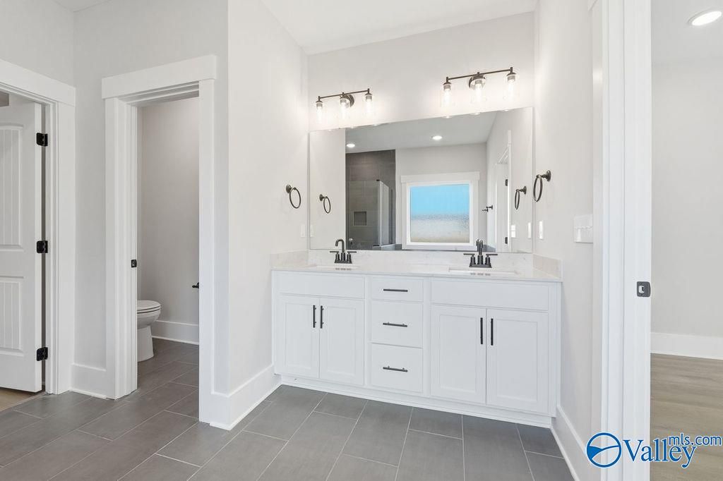 Modern master bathroom featuring double white vanity, large mirror, sconce lights, and separate toilet area in Davidson Homes The Rockford, Hartselle, Alabama