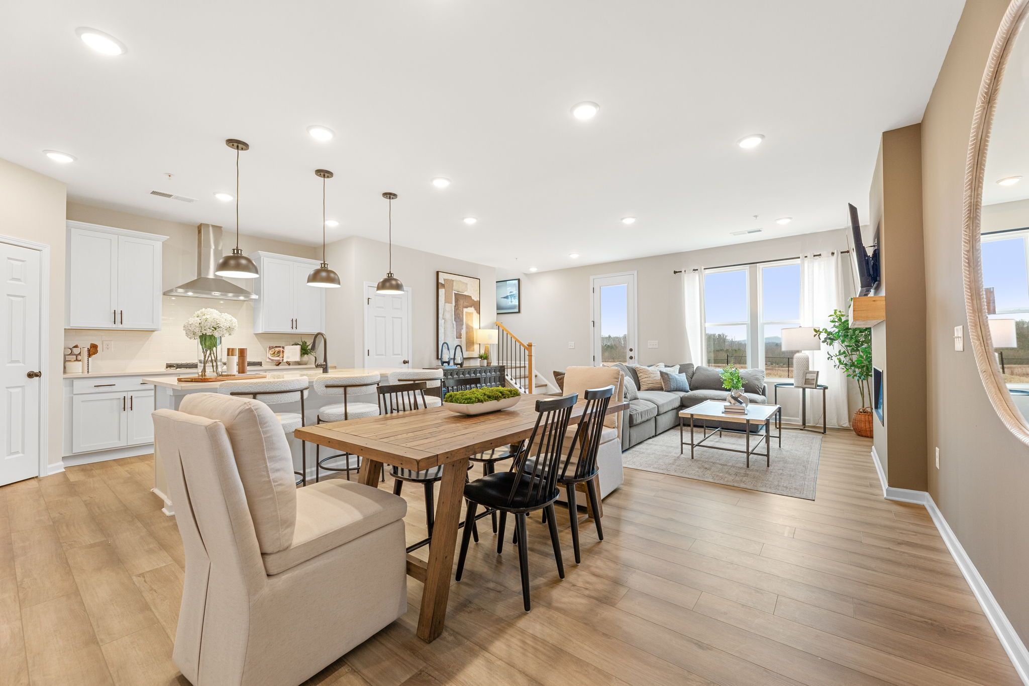 Open-concept kitchen dining living space with white cabinets, farmhouse table, beige sofa, large windows in Davidson Homes The Durham B, Cumming GA
