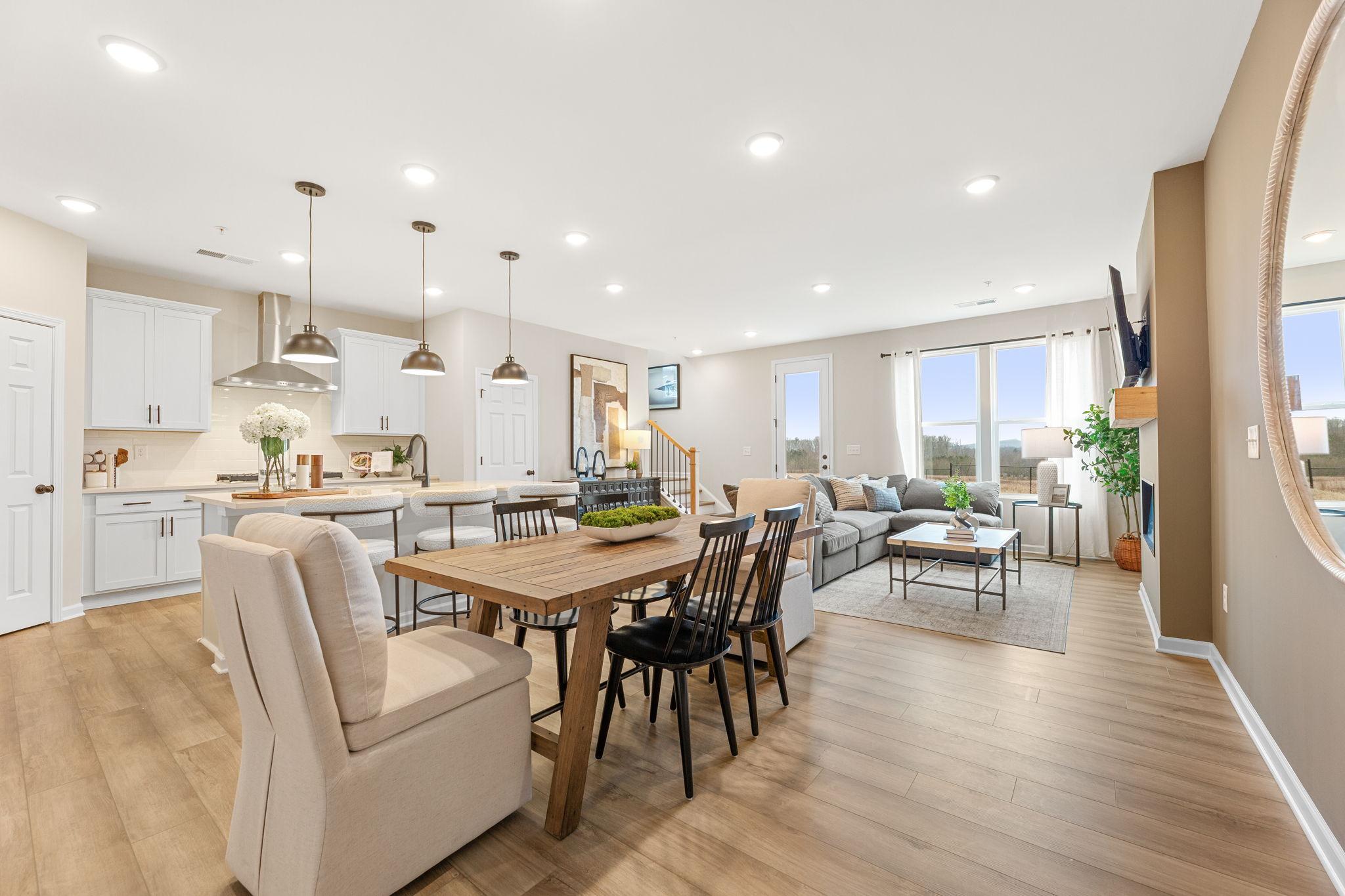 Open-concept kitchen dining living space with white cabinets, farmhouse table, beige sofa, large windows in Davidson Homes The Durham B, Cumming GA