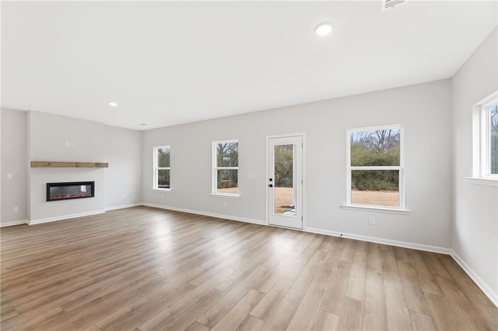 Cozy family room with stone gas fireplace, hardwood floors, large windows, and glass door in The Rabun C by Davidson Homes, Winder, GA