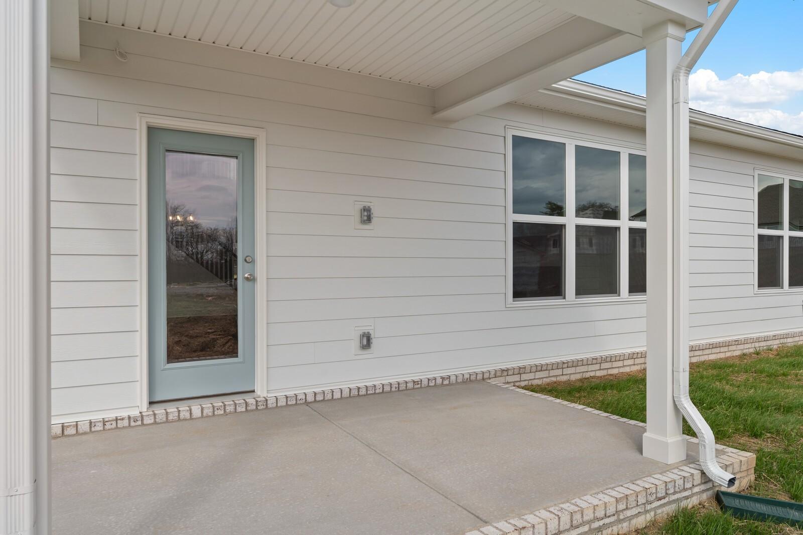 Covered back patio with glass French door, large windows, and white siding on Davidson Homes The Ridgeport in Gallatin, TN
