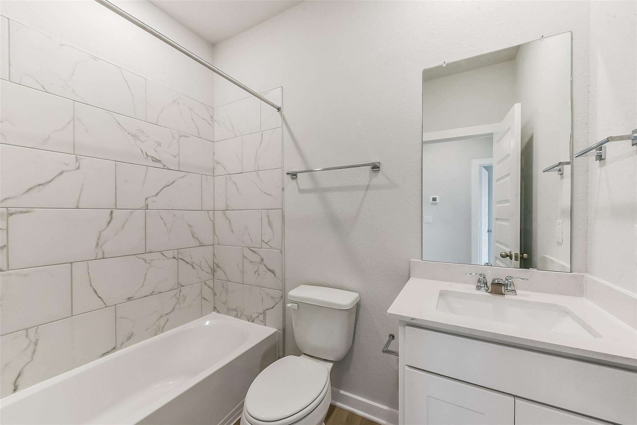 Modern bathroom with white marble subway tiles, tub-shower combo, vanity sink, and mirror in Davidson Homes The Frio G, Magnolia Texas