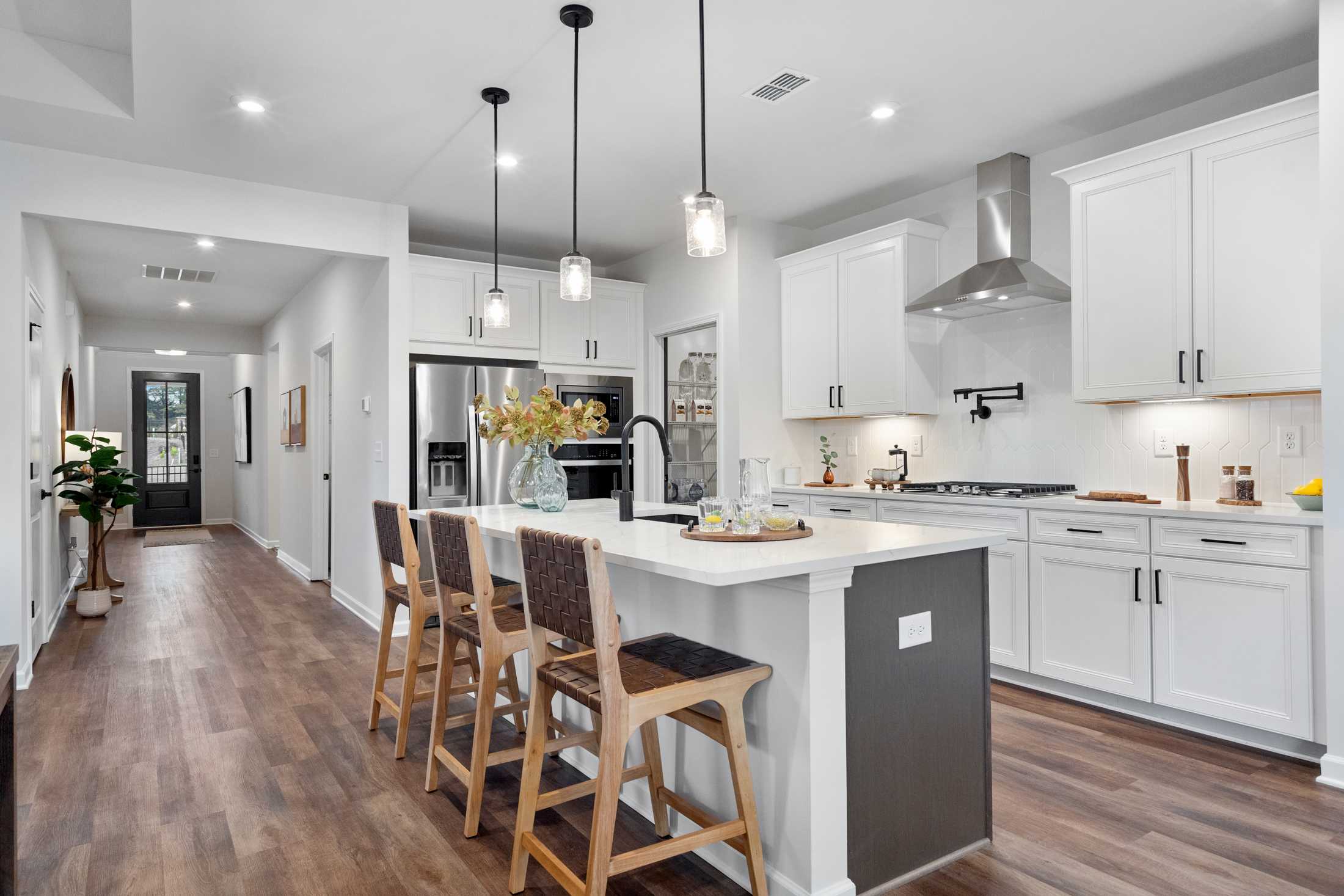 Spacious modern kitchen at Kelly Preserve in Loganville GA with white cabinets, center island, pendant lights, and hardwood floors