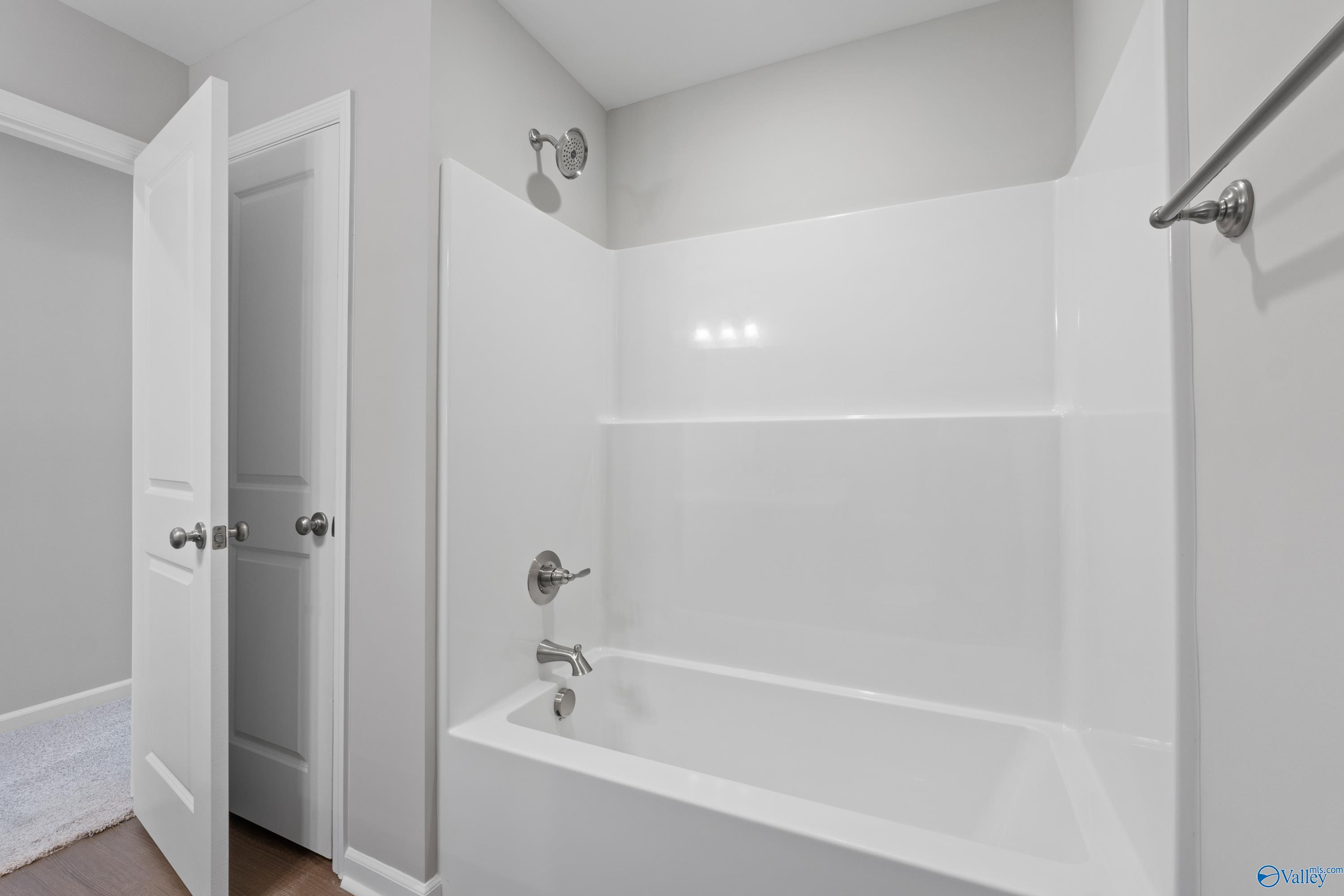 Modern white bathtub-shower combo with grab bars in gray bathroom, The Dorado floor plan by Davidson Homes in Athens, Alabama