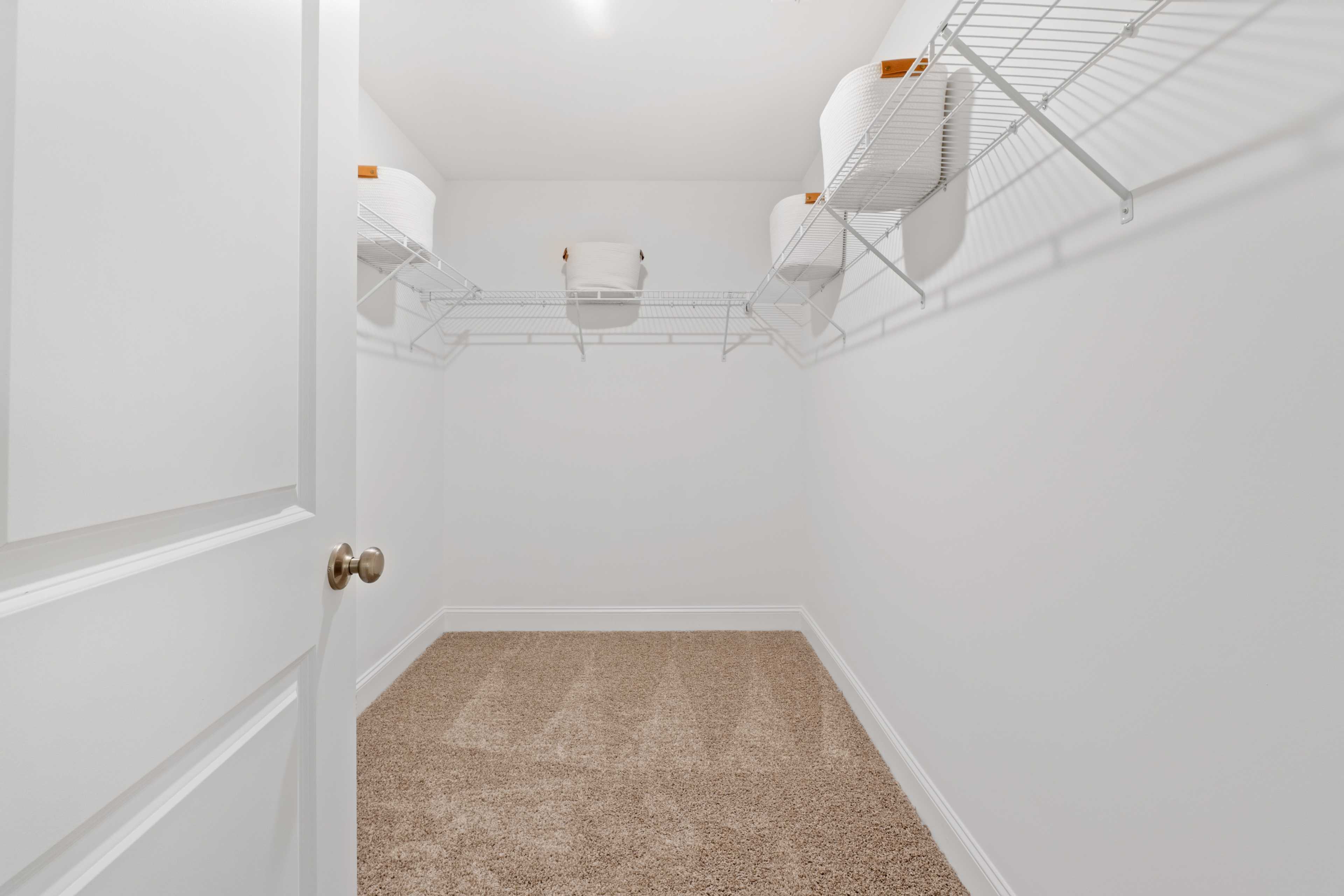 Spacious walk-in closet at Pavilion in Huntsville Alabama with white wire shelving and orange storage bins