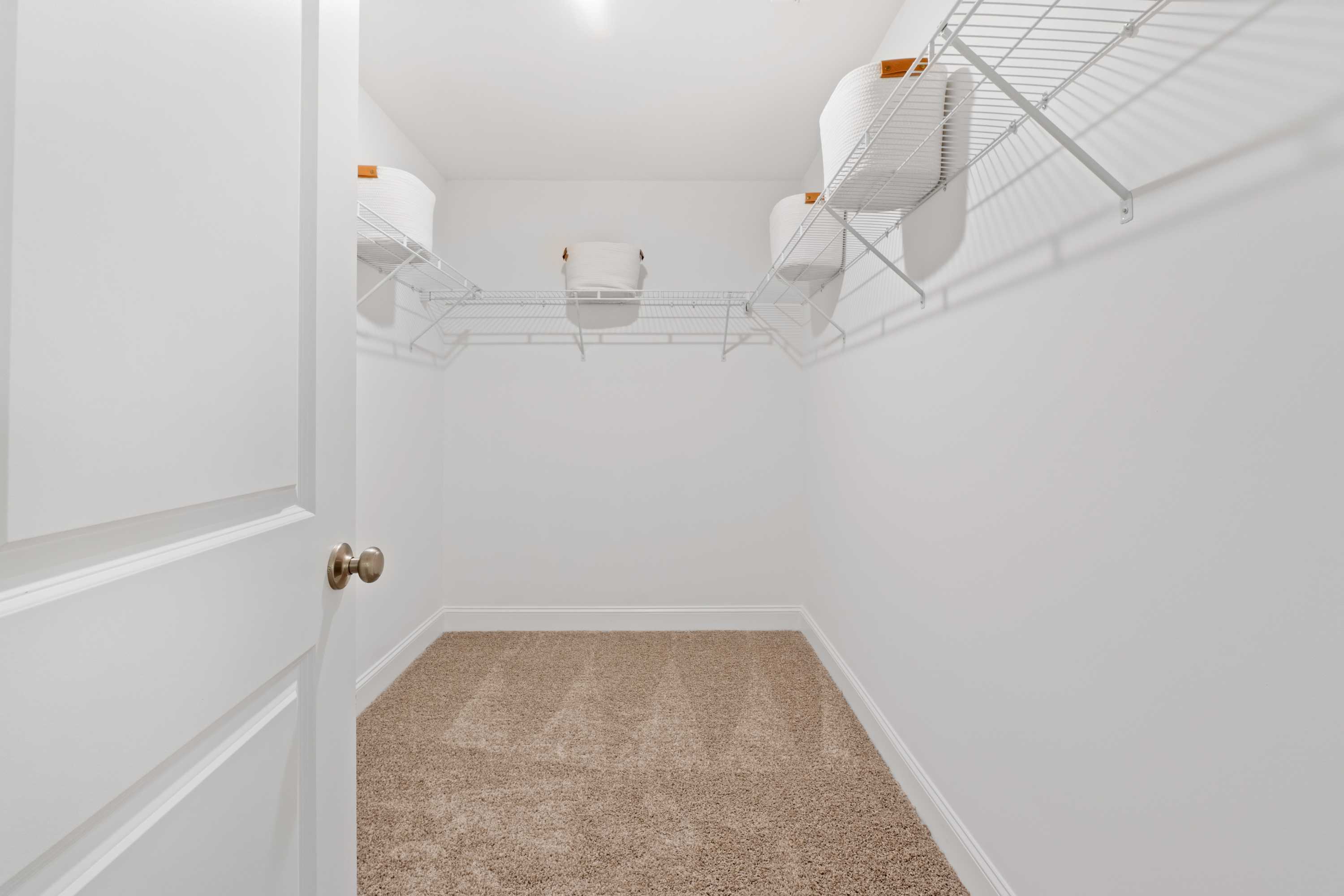 Spacious walk-in closet at Pavilion in Huntsville Alabama with white wire shelving and orange storage bins