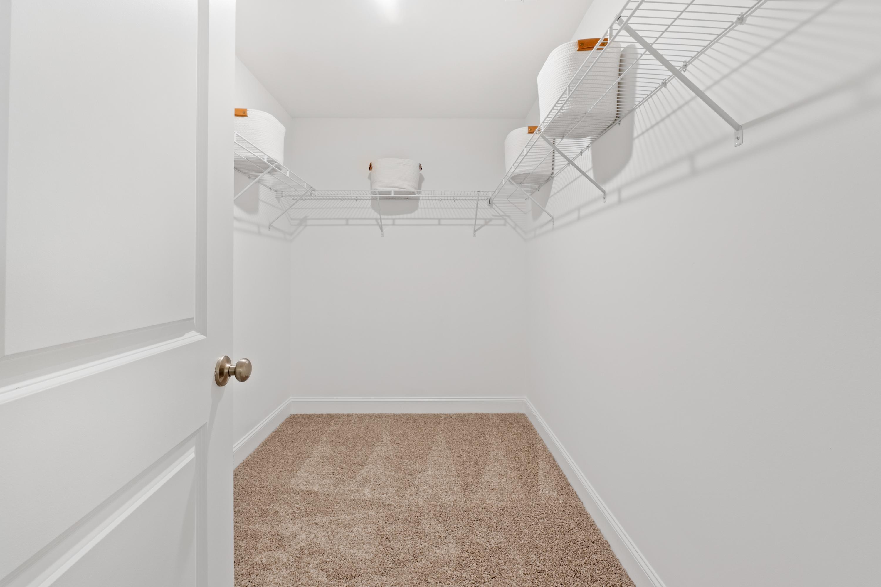Spacious walk-in closet at Pavilion in Huntsville Alabama with white wire shelving and orange storage bins