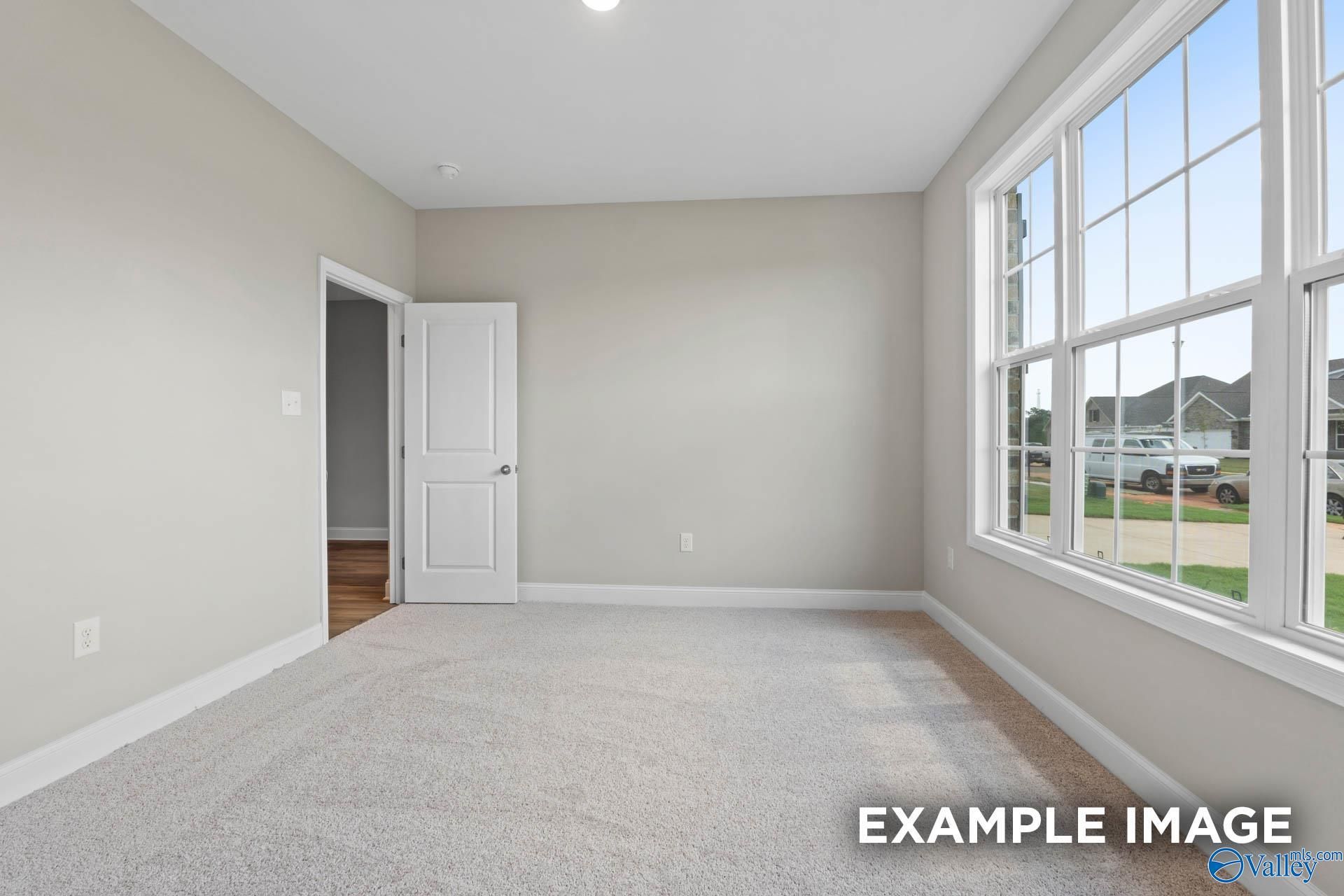 Bright empty bedroom with neutral beige walls, large windows, and plush carpet in Davidson Homes The Montgomery, Meridianville, Alabama