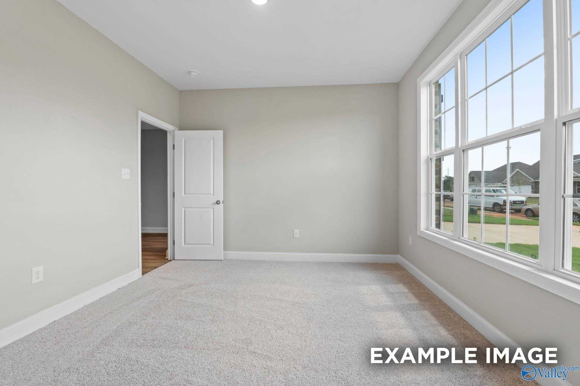 Bright empty bedroom with neutral beige walls, large windows, and plush carpet in Davidson Homes The Montgomery, Meridianville, Alabama