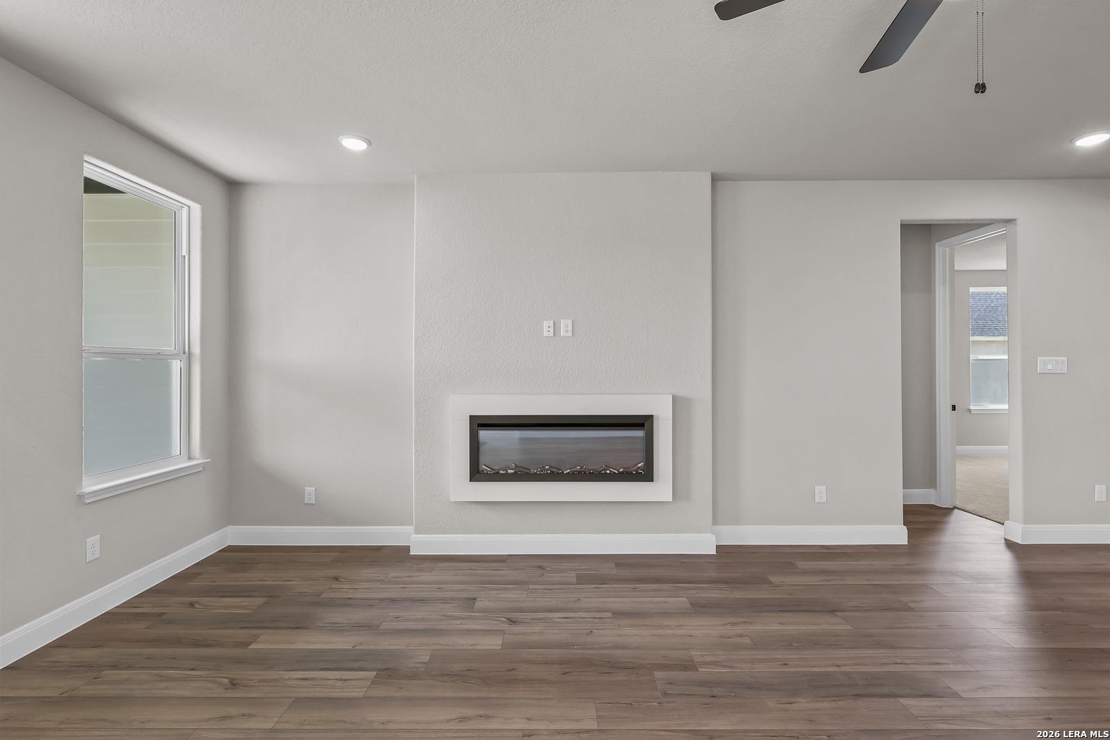 Bright living room with modern electric fireplace, wood-look flooring, and ceiling fan in Davidson Homes The Foster E, Castroville, Texas