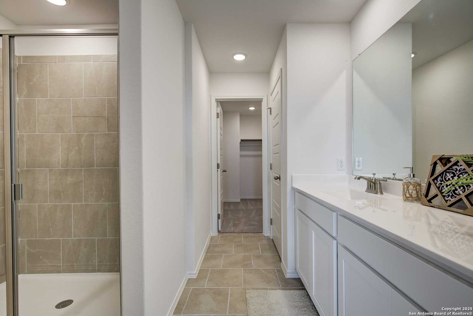 Elegant master bathroom with tiled walk-in shower, white quartz vanity, and linen closet in Davidson Homes The Trinity A, San Antonio