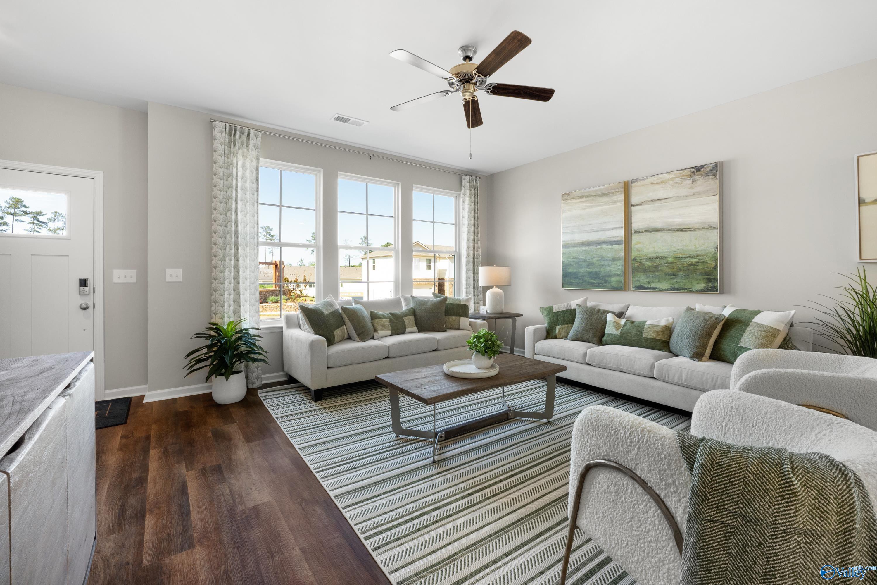 Bright living room with beige sofas, green pillows, ceiling fans, large windows, and abstract art in Davidson Homes The Stella, Madison Alabama