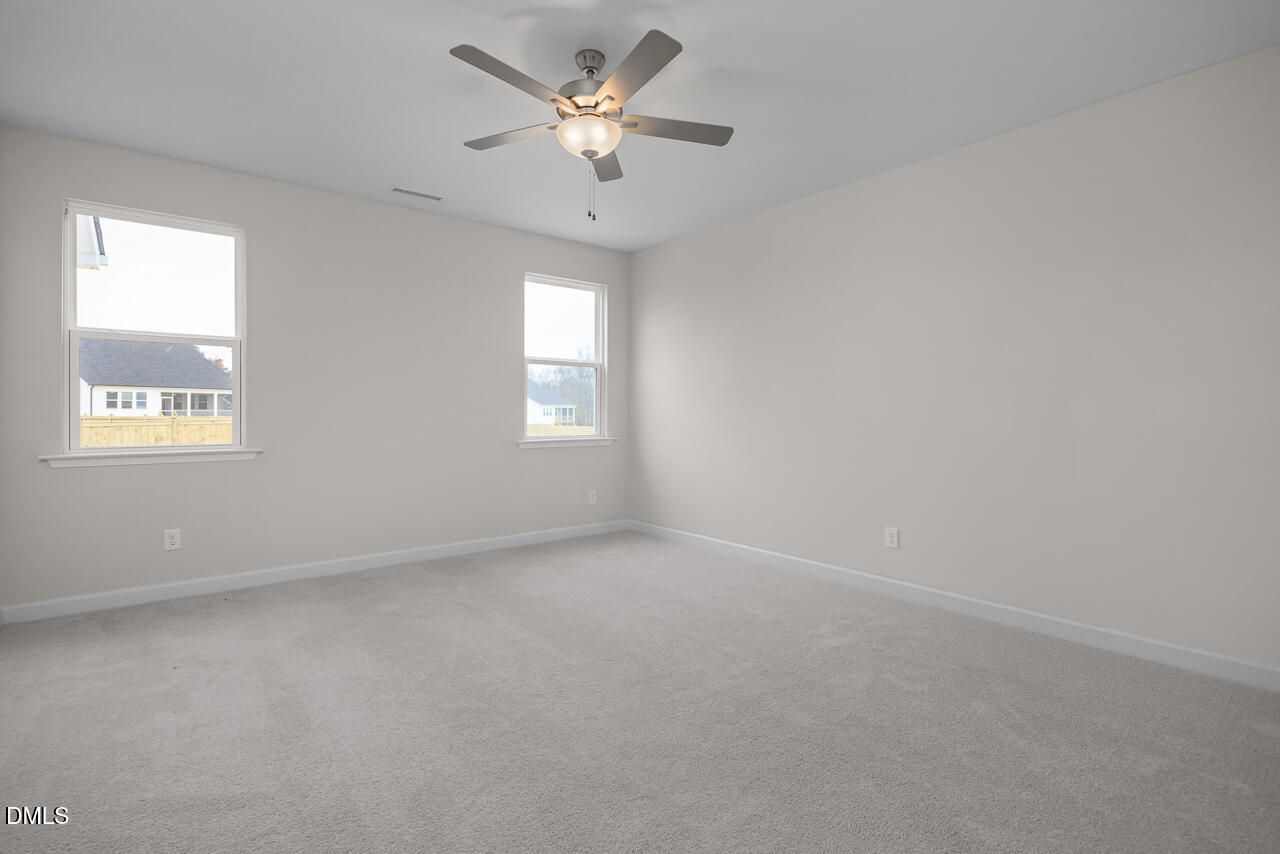 Empty bedroom with ceiling fan, large windows, beige walls, and carpeted floor in Davidson Homes The Cypress D II, Angier, NC