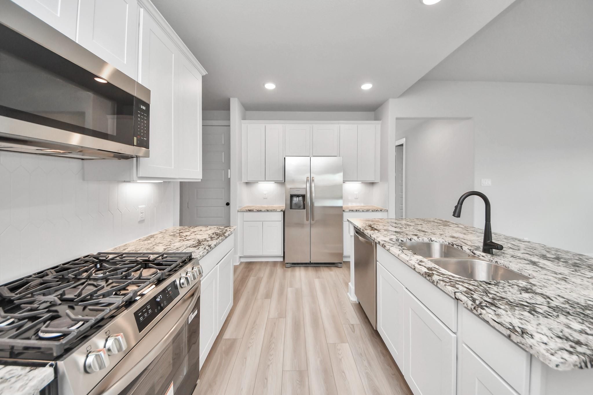 Modern kitchen with white cabinets, granite countertops, and stainless appliances in The Laguna C floor plan, Sunterra, Katy.