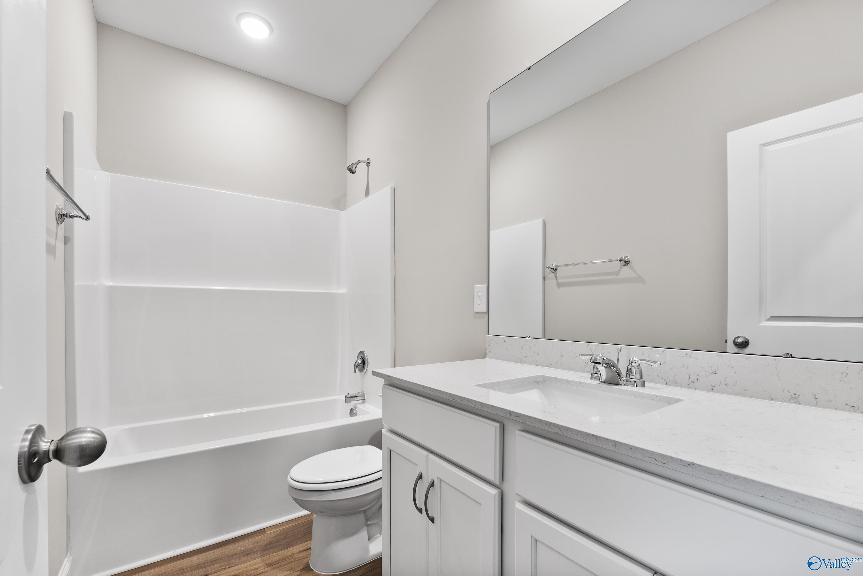 Bright secondary bathroom with white tub-shower combo, single vanity sink, toilet, and mirror in Davidson Homes The Daphne C, Harvest, AL